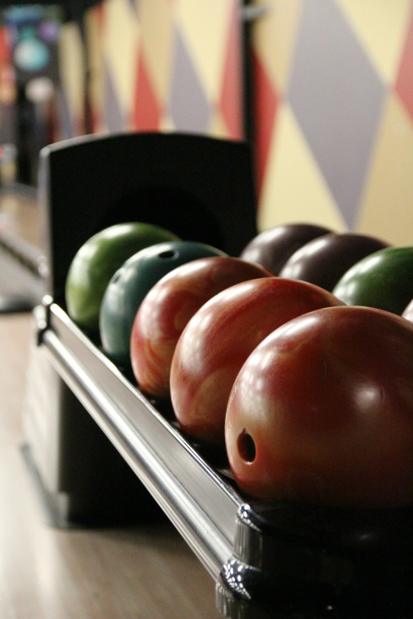 A bowling ball rack with several different colored bowling balls lined up in a bowling alley.