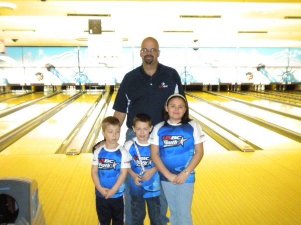 Scott Gielda with three children at a bowling alley, all wearing matching team shirts.
