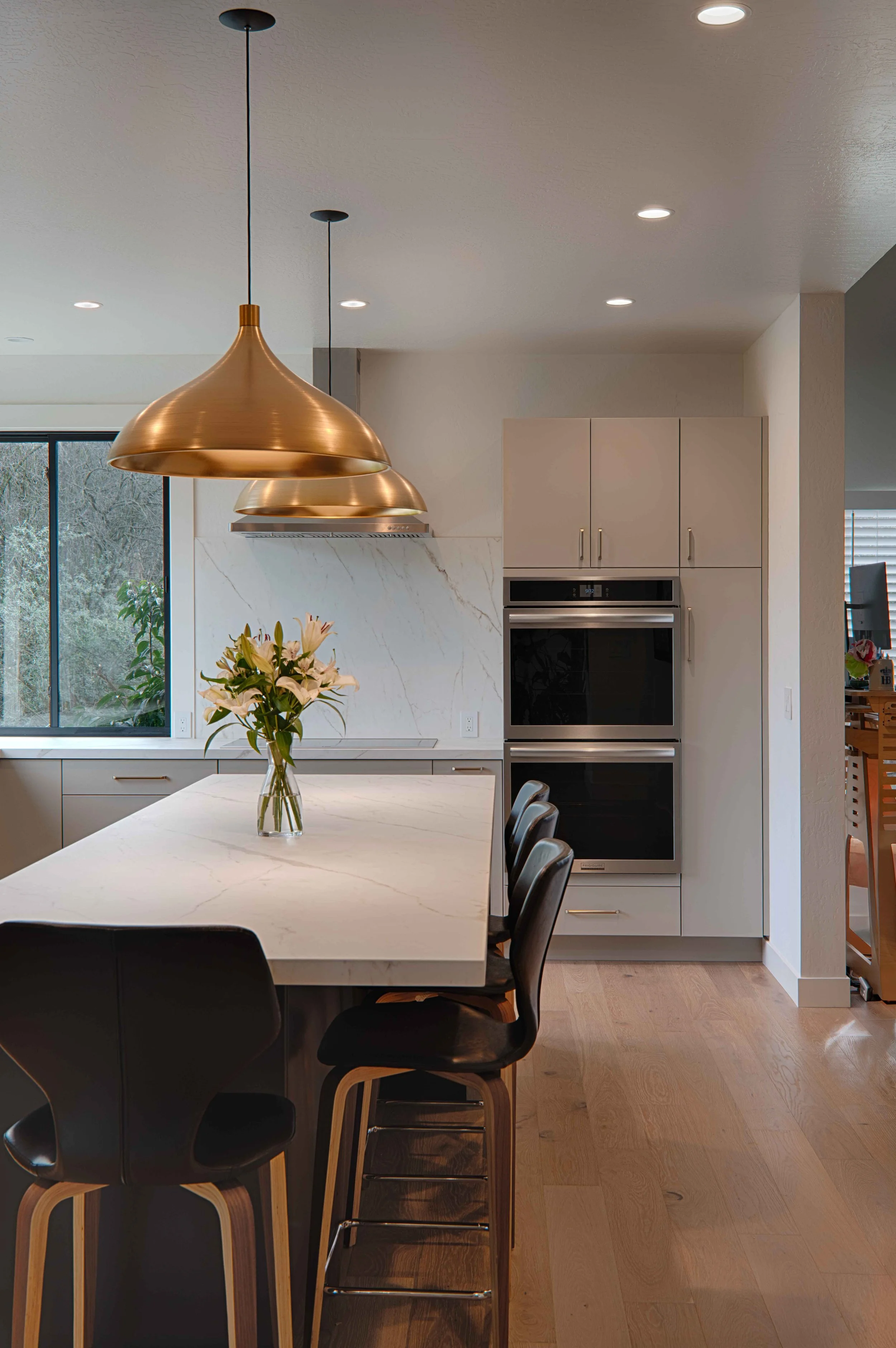 Modern kitchen with a white marble island, black chairs, gold pendant lights, and a vase of flowers