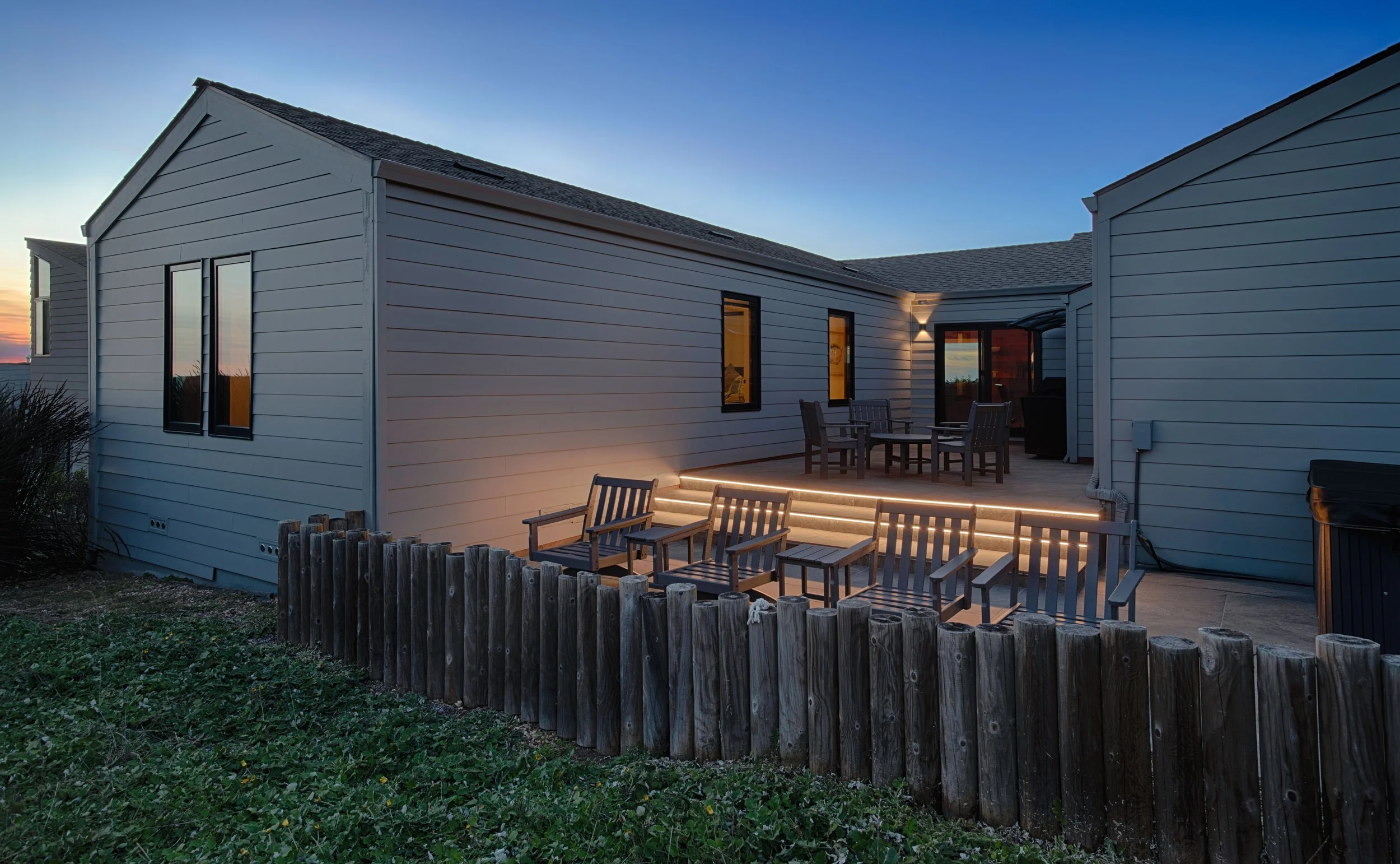 Backyard patio with outdoor seating, illuminated stairs, and a wooden fence at sunset.
