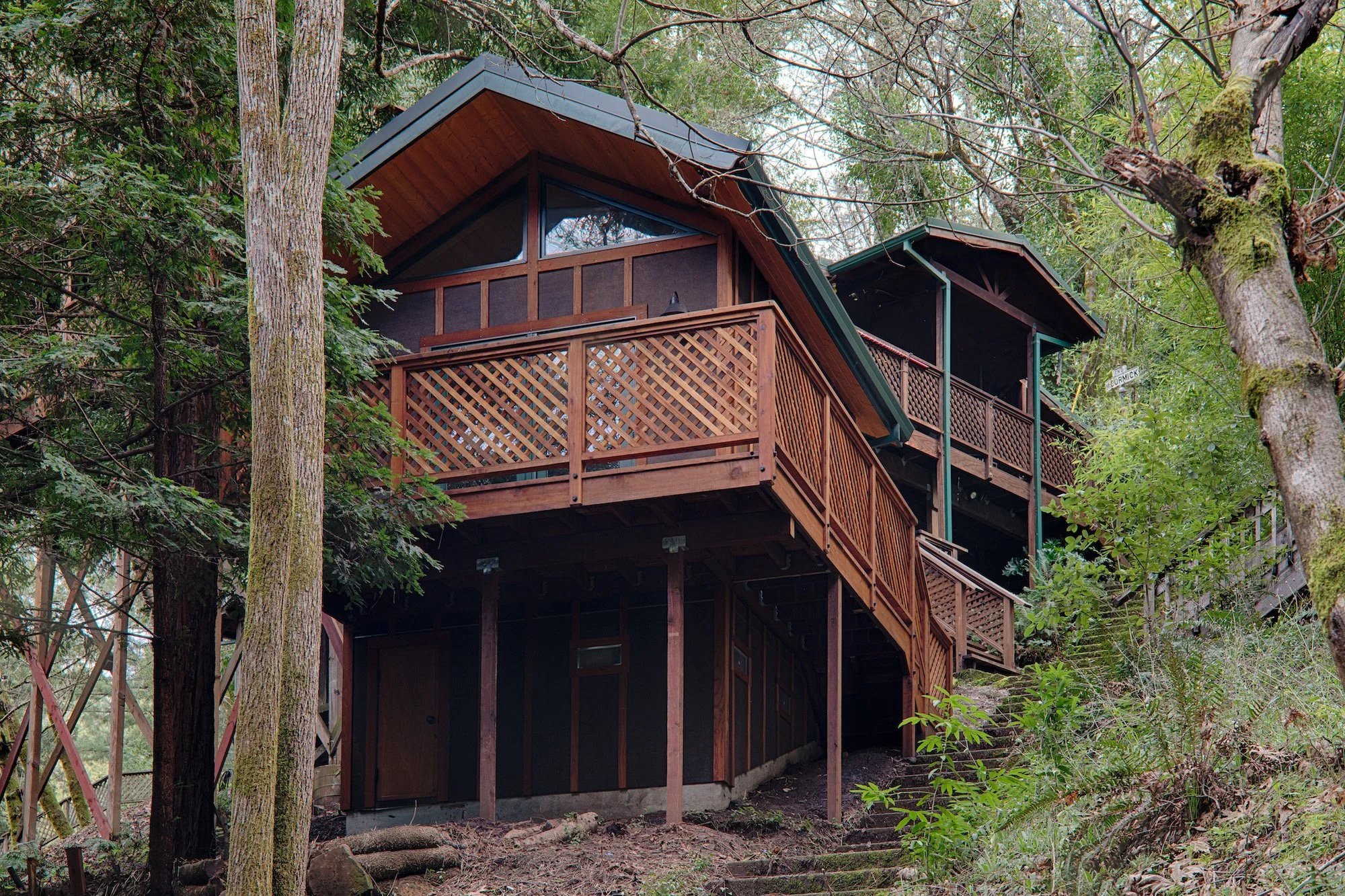 A multi-level wooden house built on a hillside surrounded by trees and greenery.