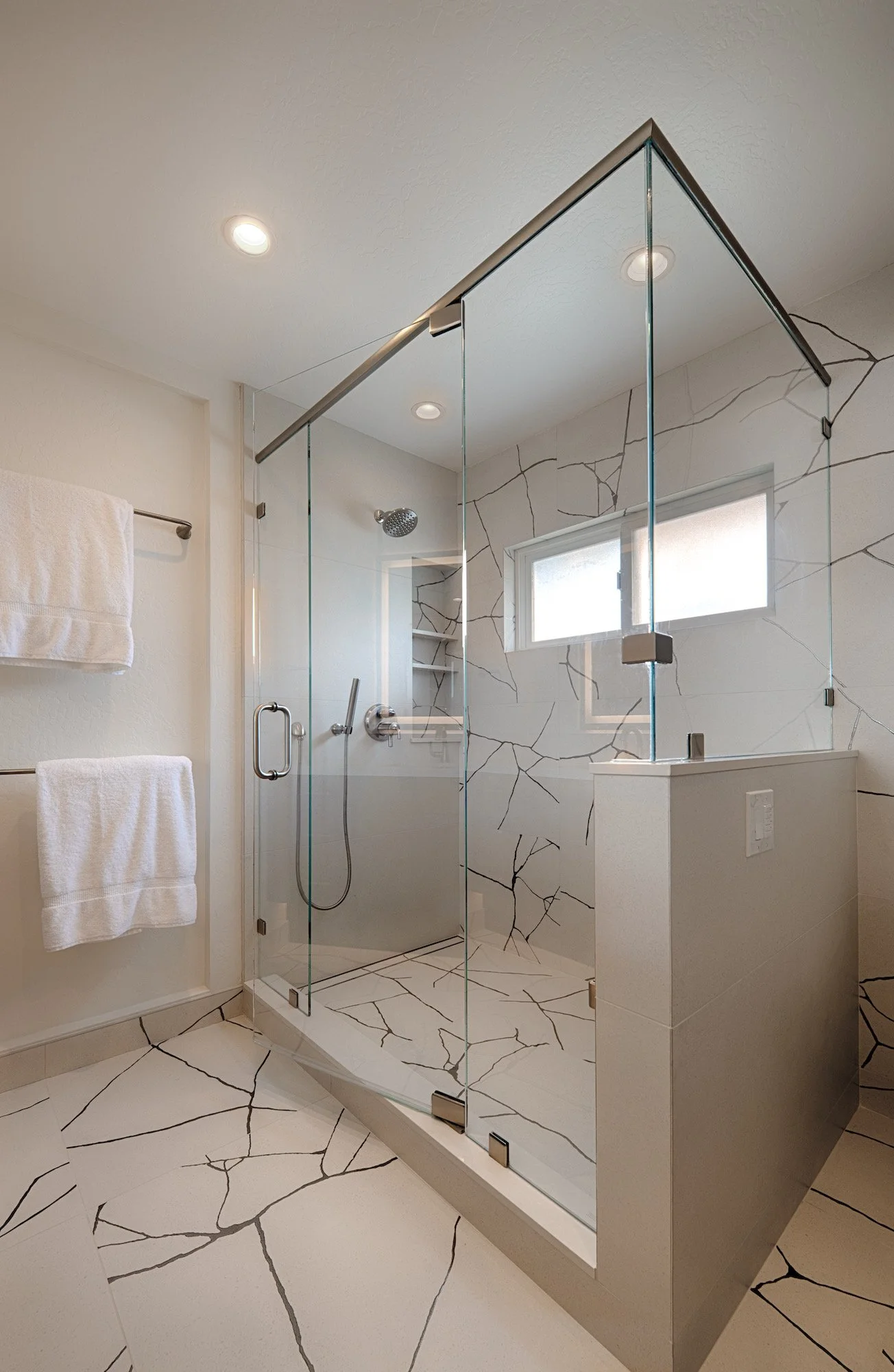 Modern bathroom shower with glass enclosure, marble-like walls, and tiled floor with black veining pattern.