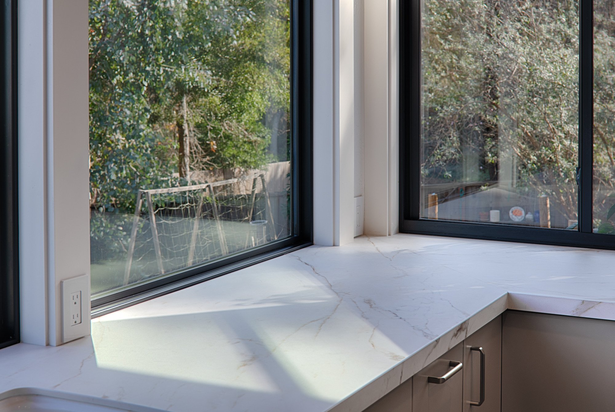 Kitchen window with a marble countertop, outside view of trees, and a soccer goal in the backyard.