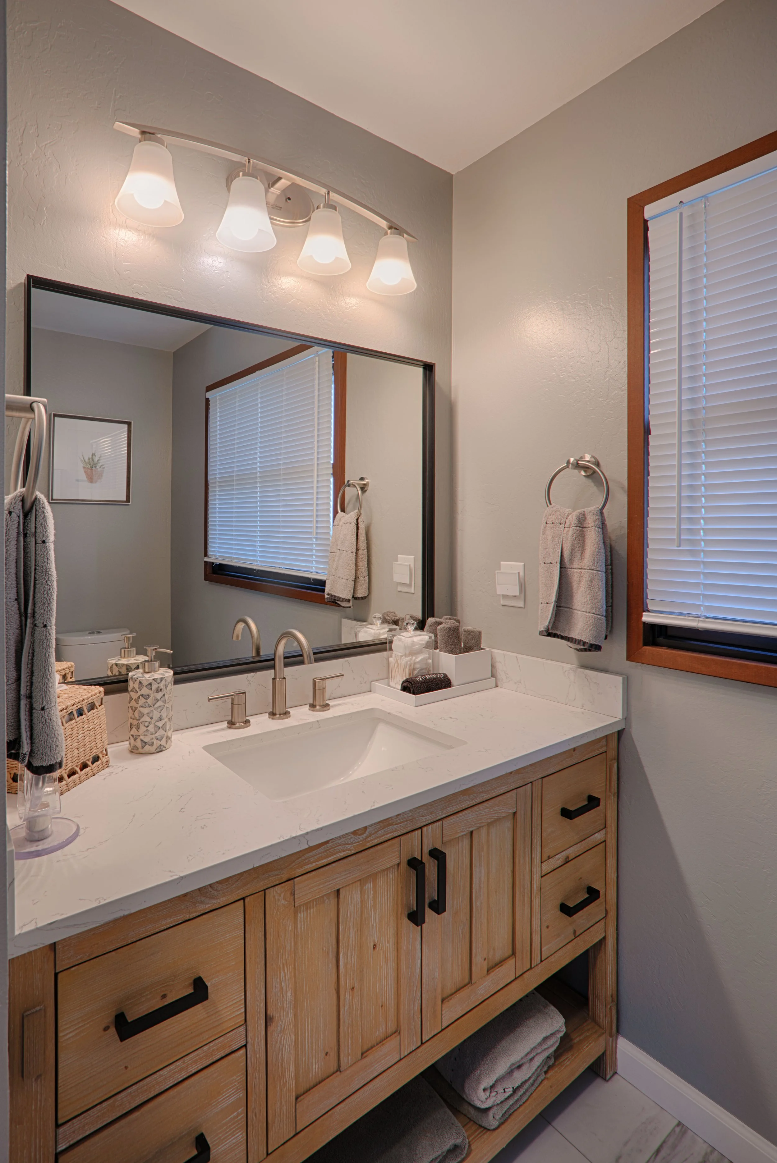 Bathroom vanity with a large mirror, wooden cabinet, and modern faucet, decorated with soap dispensers, toiletries, and towels.