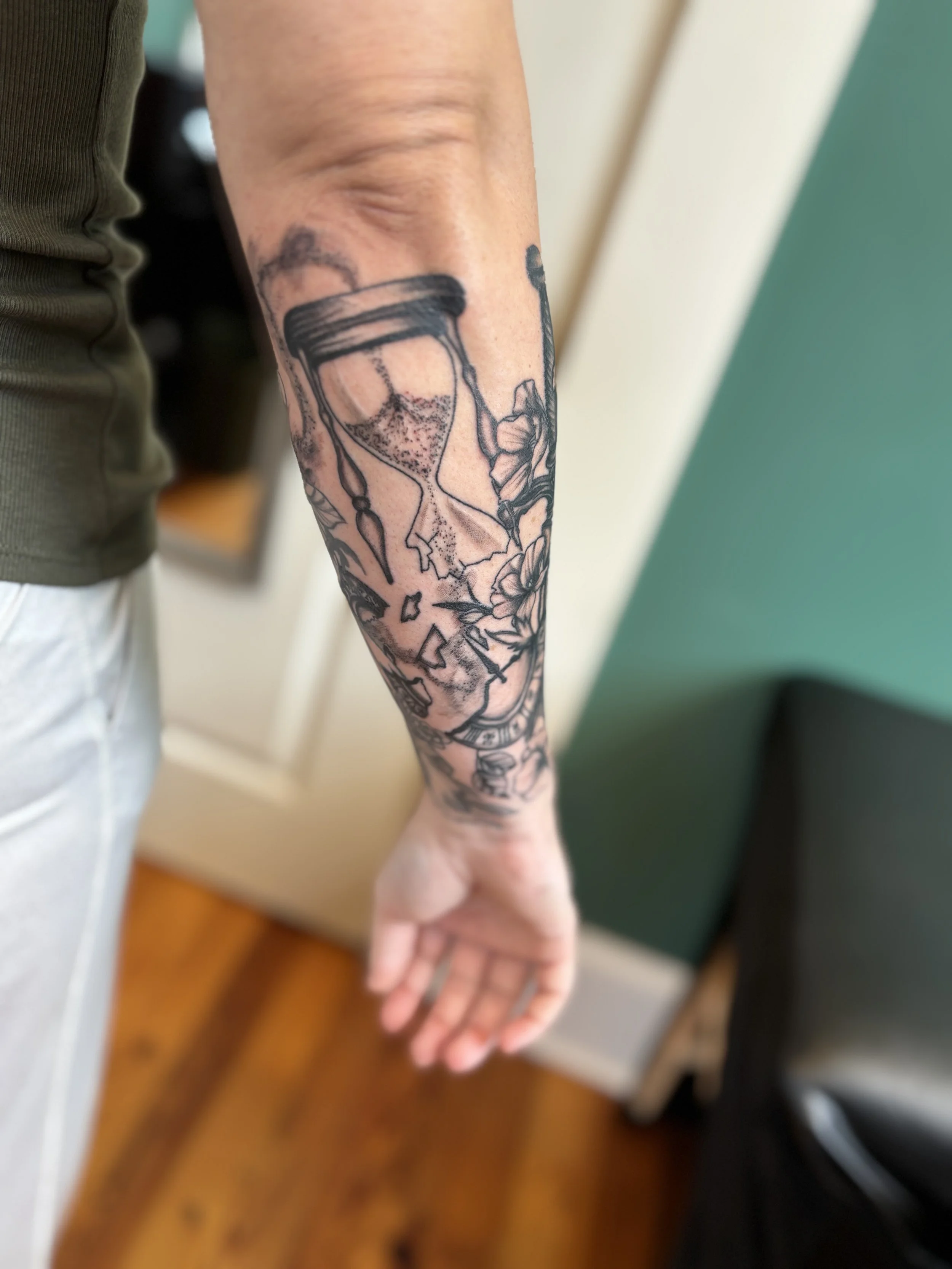 Tattoo of an hourglass and flowers on person's arm.