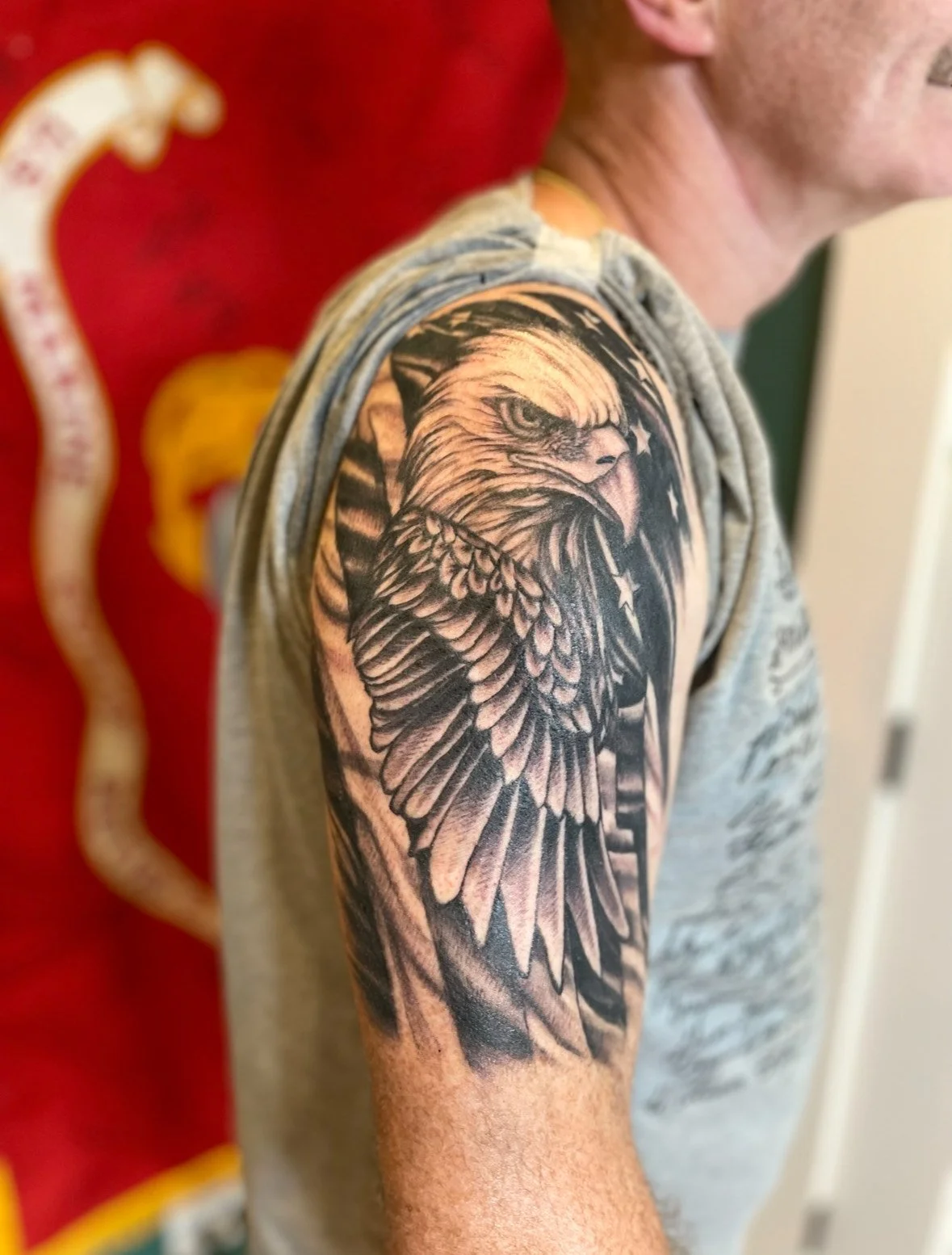 Black and gray tattoo of an eagle's head on a man's upper arm and shoulder.