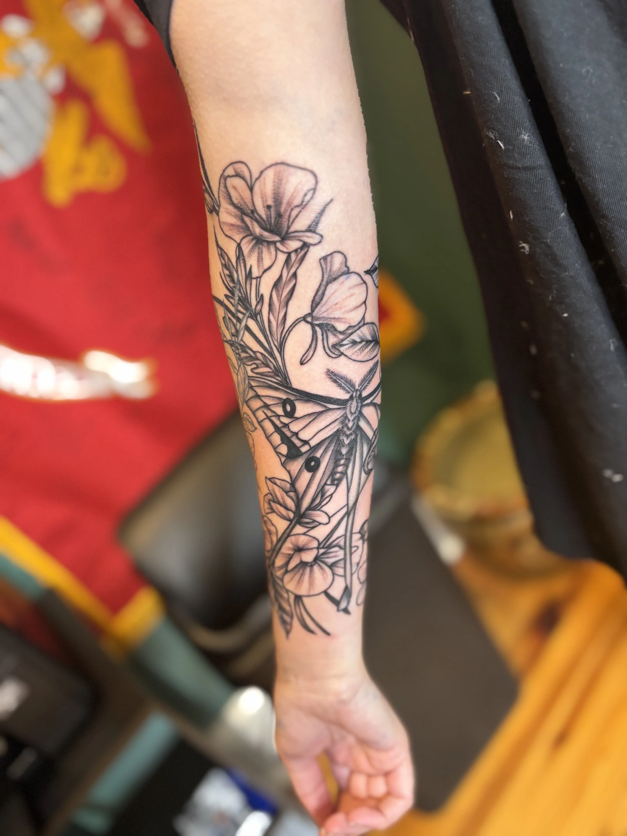 Black ink floral and butterfly tattoo on person's forearm.