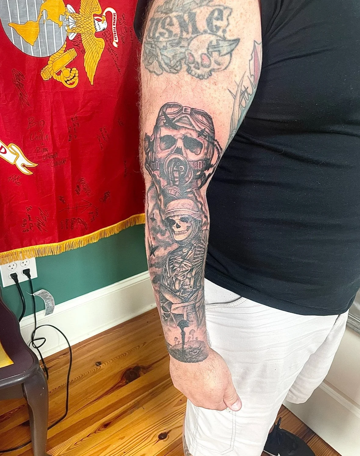 Tattoo of a skull wearing a helmet with goggles, a snake, and a skeleton boy in military attire on a person's arm.