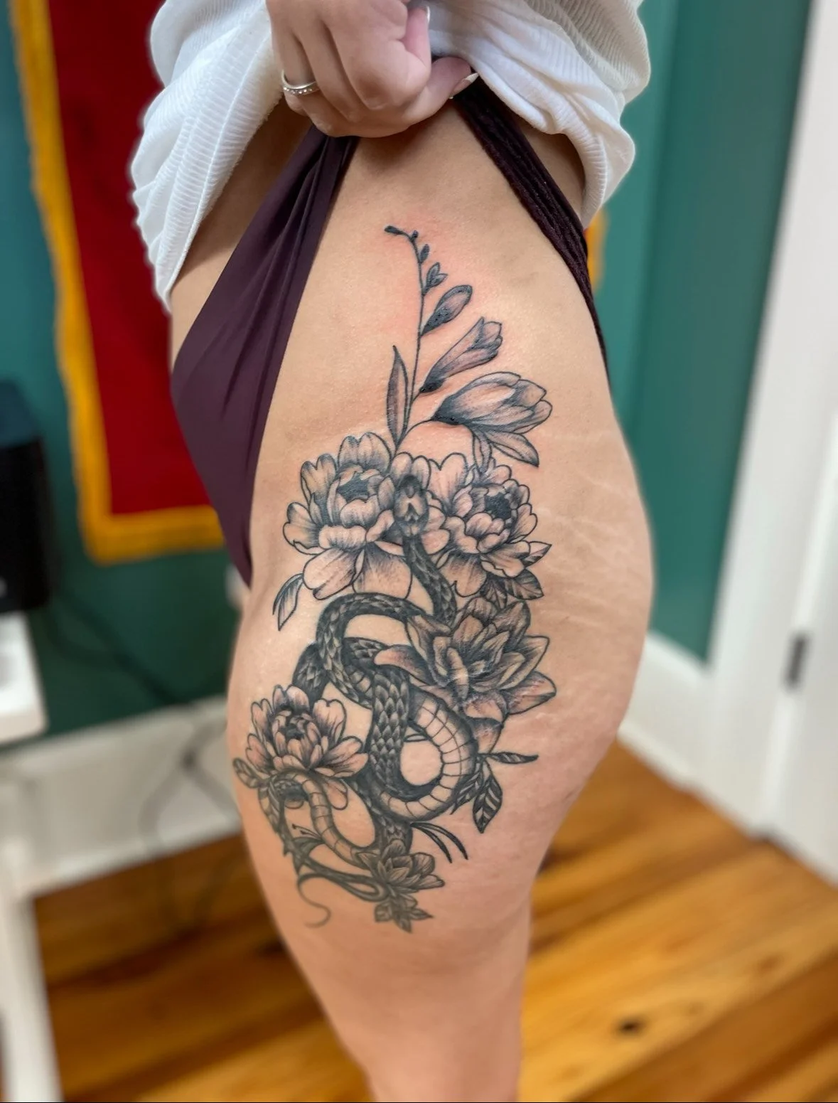 Black and gray floral tattoo featuring flowers, leaves, and a snake on a person's upper thigh.