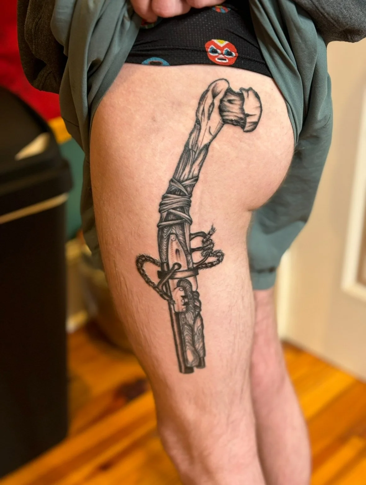 Black and gray tattoo of a sword wrapped with a rope, with a carved handle, on person's thigh.