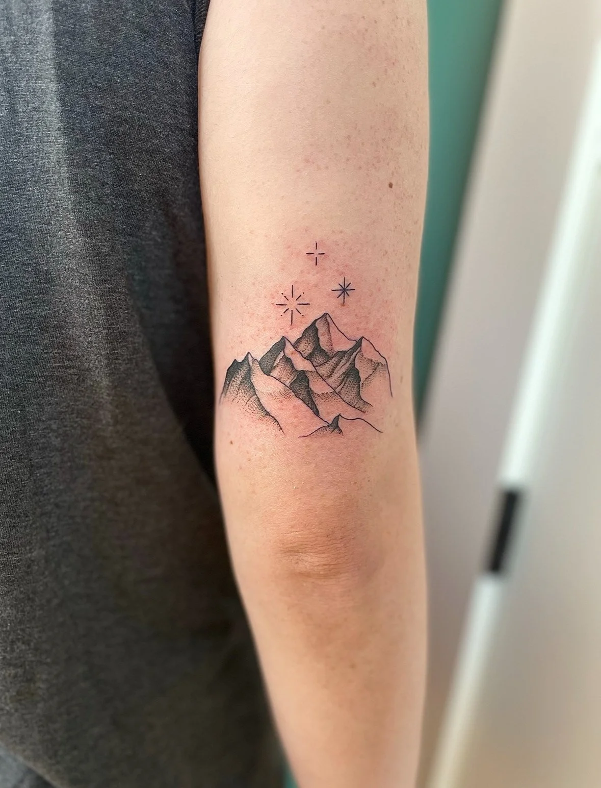 Tattoo of mountain peaks with stars above on a person's inner forearm.