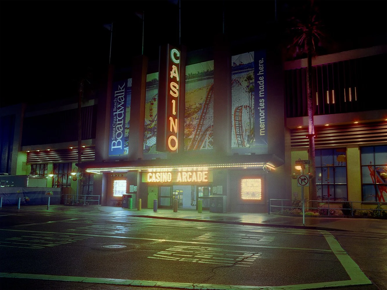 Night view of Casino Arcade with neon signs, palm trees, and a roller coaster poster, in a lively area with street markings and a no U-turn sign.