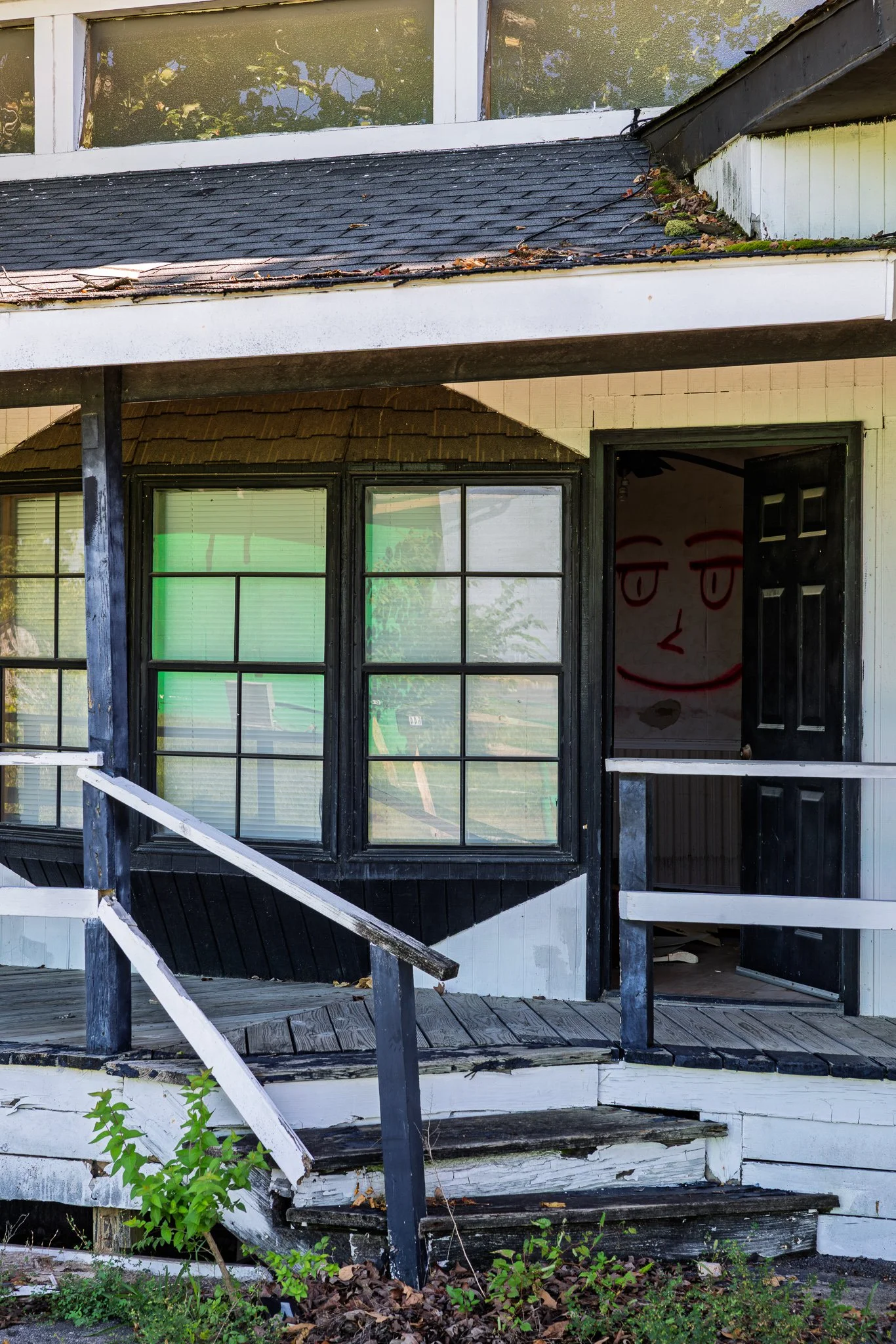 Alpine Haus Motel balcony with rusted railing. Door open with graffiti inside the room wall.