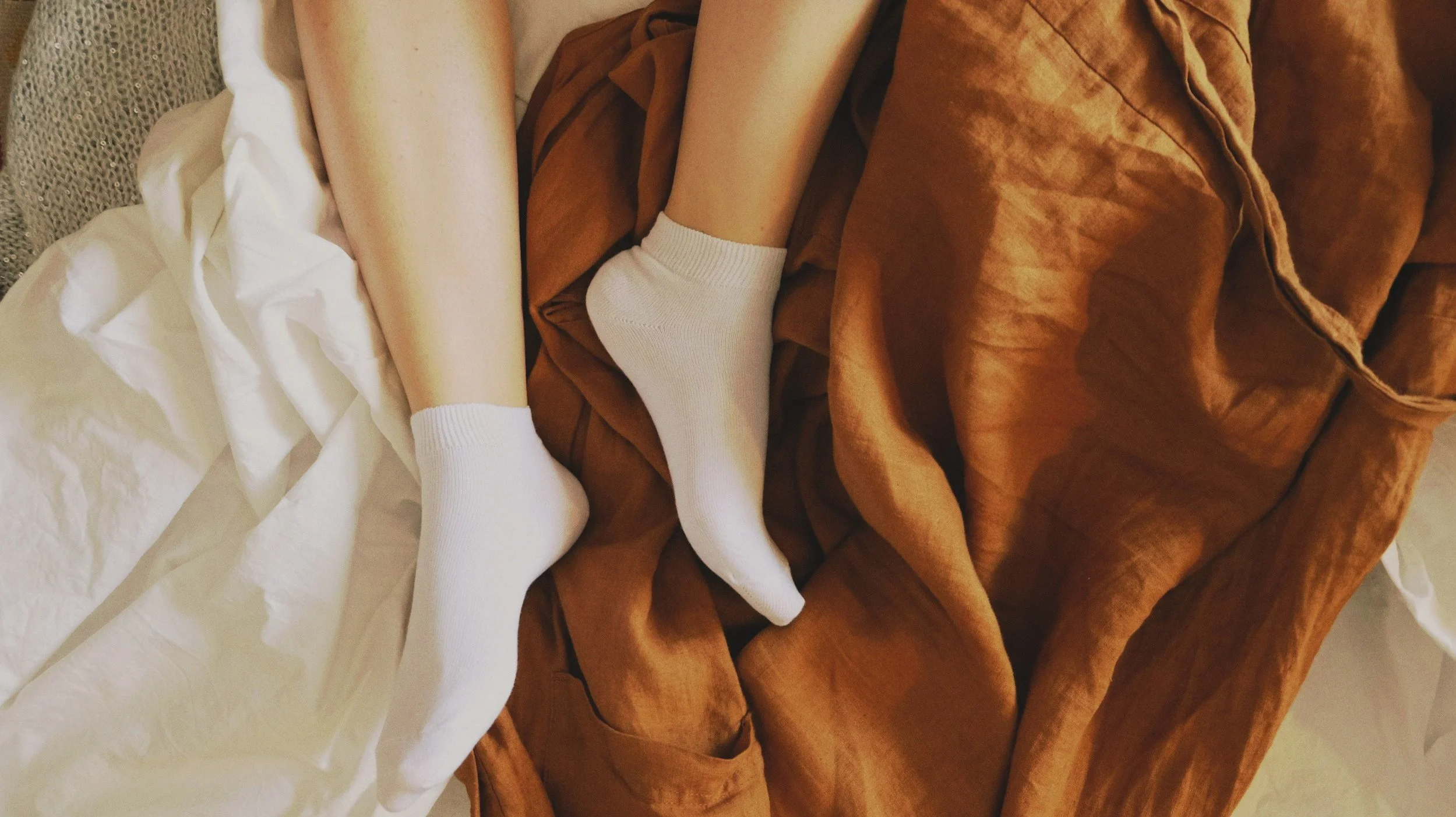 Editorial photograph of woman wrapped in cozy blanket in soft shadows, symbolizing rest and renewal during the menstrual phase.