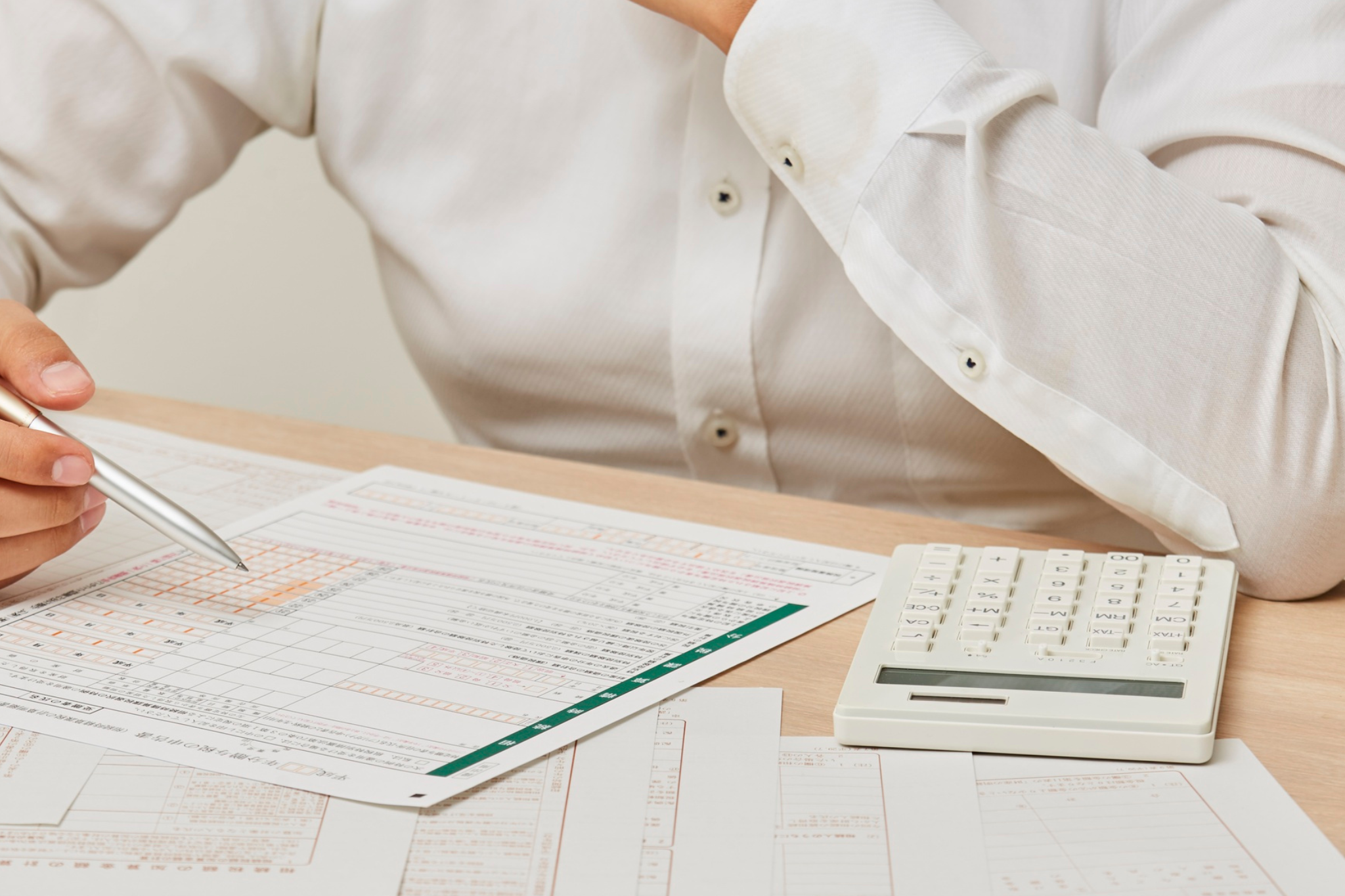 Contractor reviews construction financial reports, cost documents, and a calculator to analyze job performance beyond gross margin, identifying labor overruns, overhead costs, and profit issues before they impact overall business profitability.