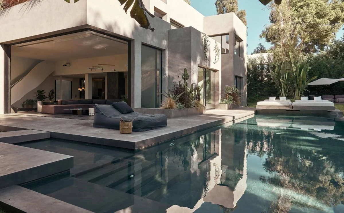 Modern house with a swimming pool, outdoor lounge area, and various plants and trees in the yard.