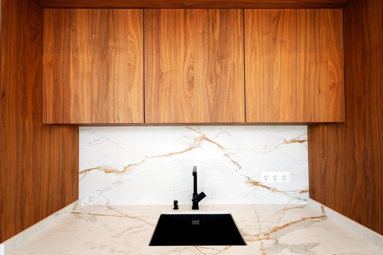 Modern kitchen with wooden cabinets, white marble backsplash with brown veins, and a black undermount sink with black faucet.