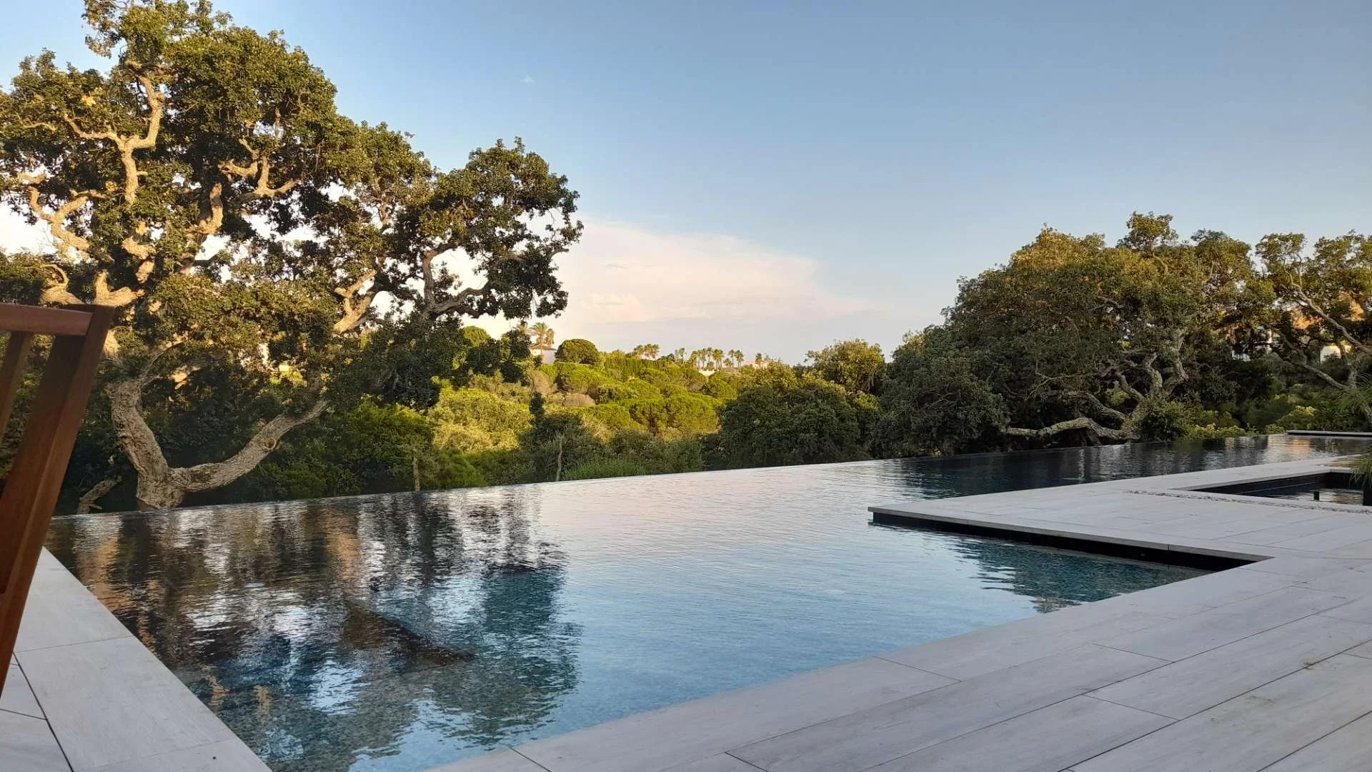 View of an infinity pool overlooking lush green trees and a blue sky with light clouds.