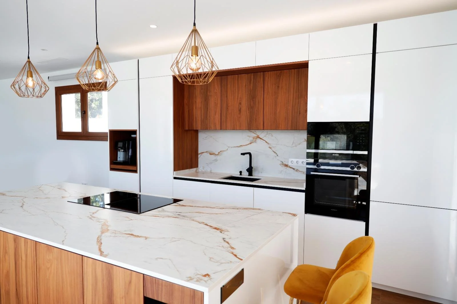 Modern kitchen with white cabinets, wooden accents, marble countertops, a black stovetop, and modern pendant lights.
