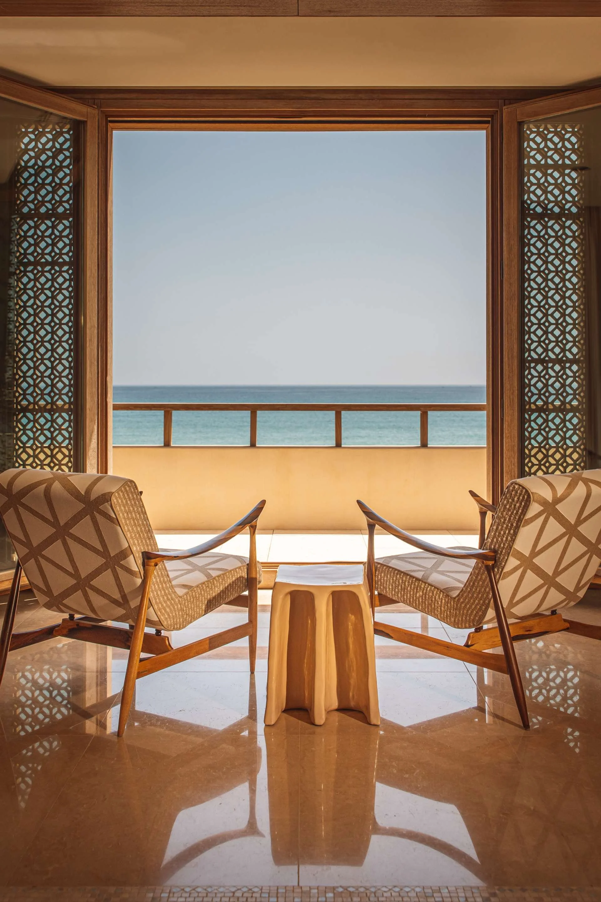 Two modern armchairs facing a balcony with a view of the ocean, seen through an open sliding door in a tropical or beach resort setting.