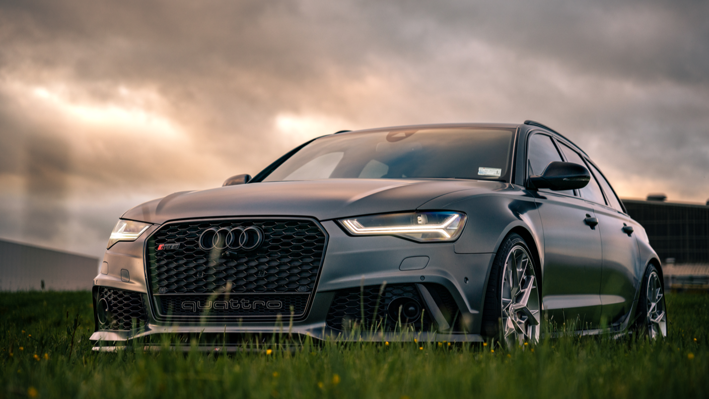 A black Audi RS3 sedan parked on a grassy area with a cloudy sky in the background.