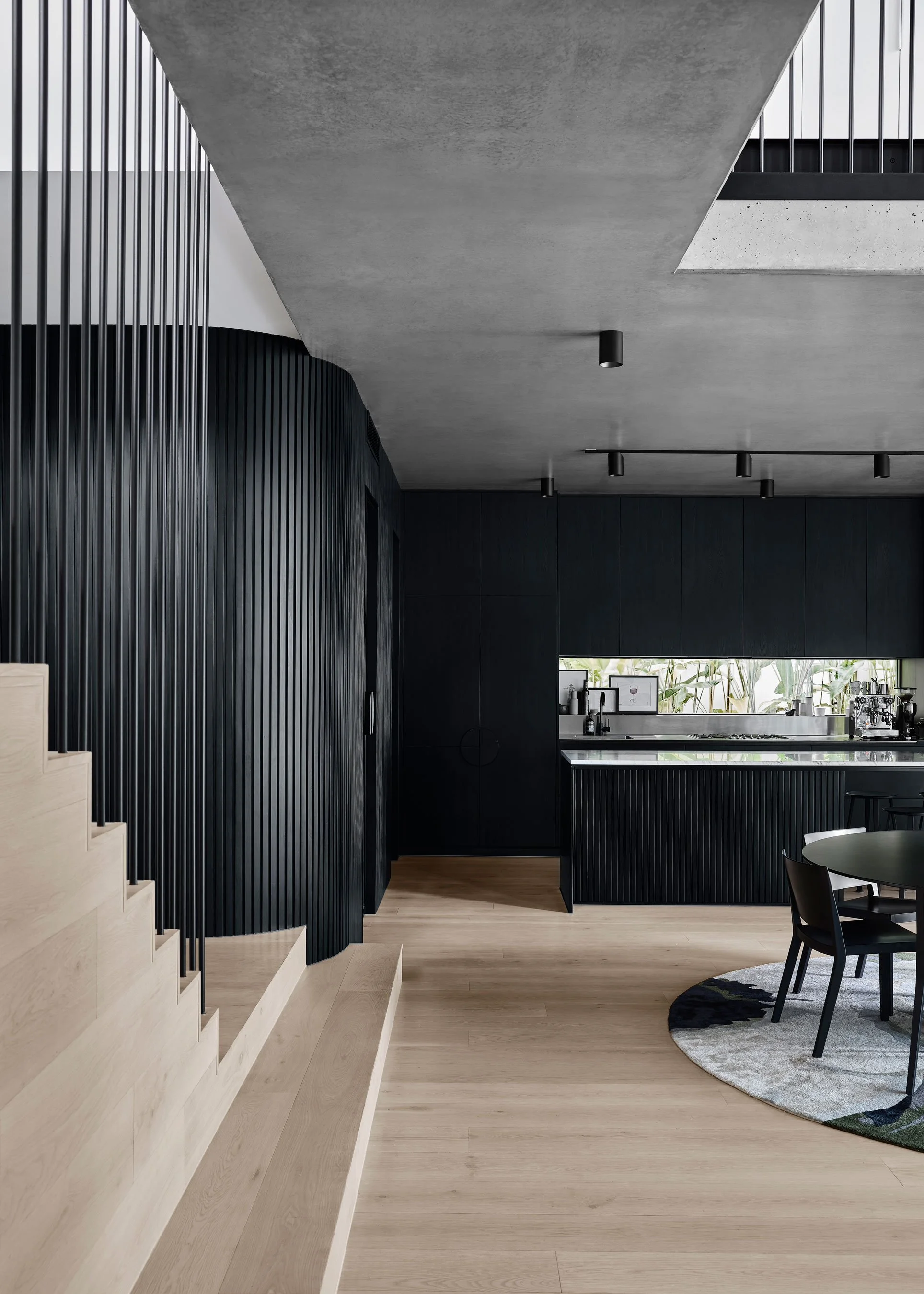 Modern interior with black and wood accents, a staircase on the left, and a black kitchen counter with a window backdrop.