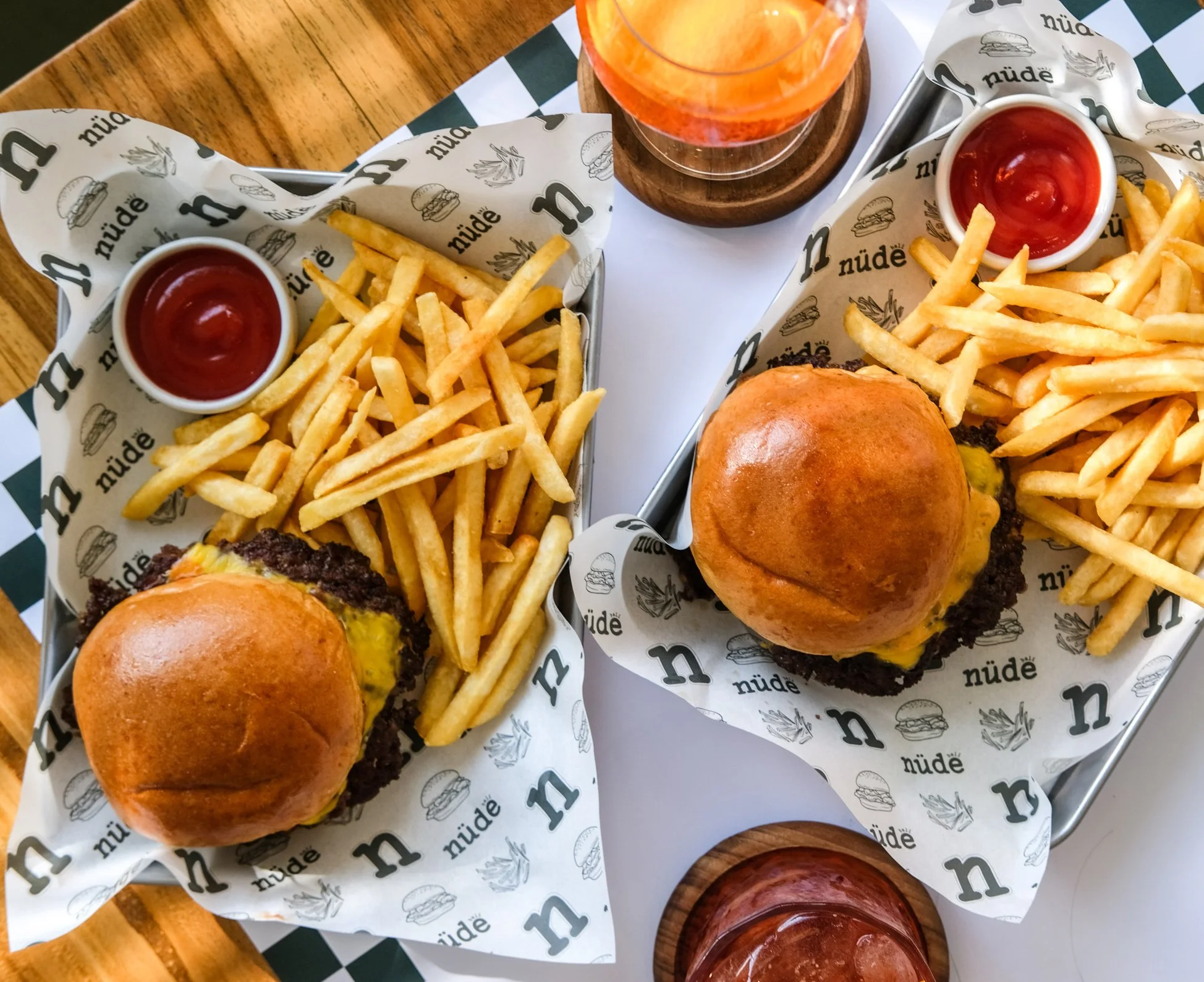 Two trays with cheeseburgers, French fries, ketchup, and drinks on a table.