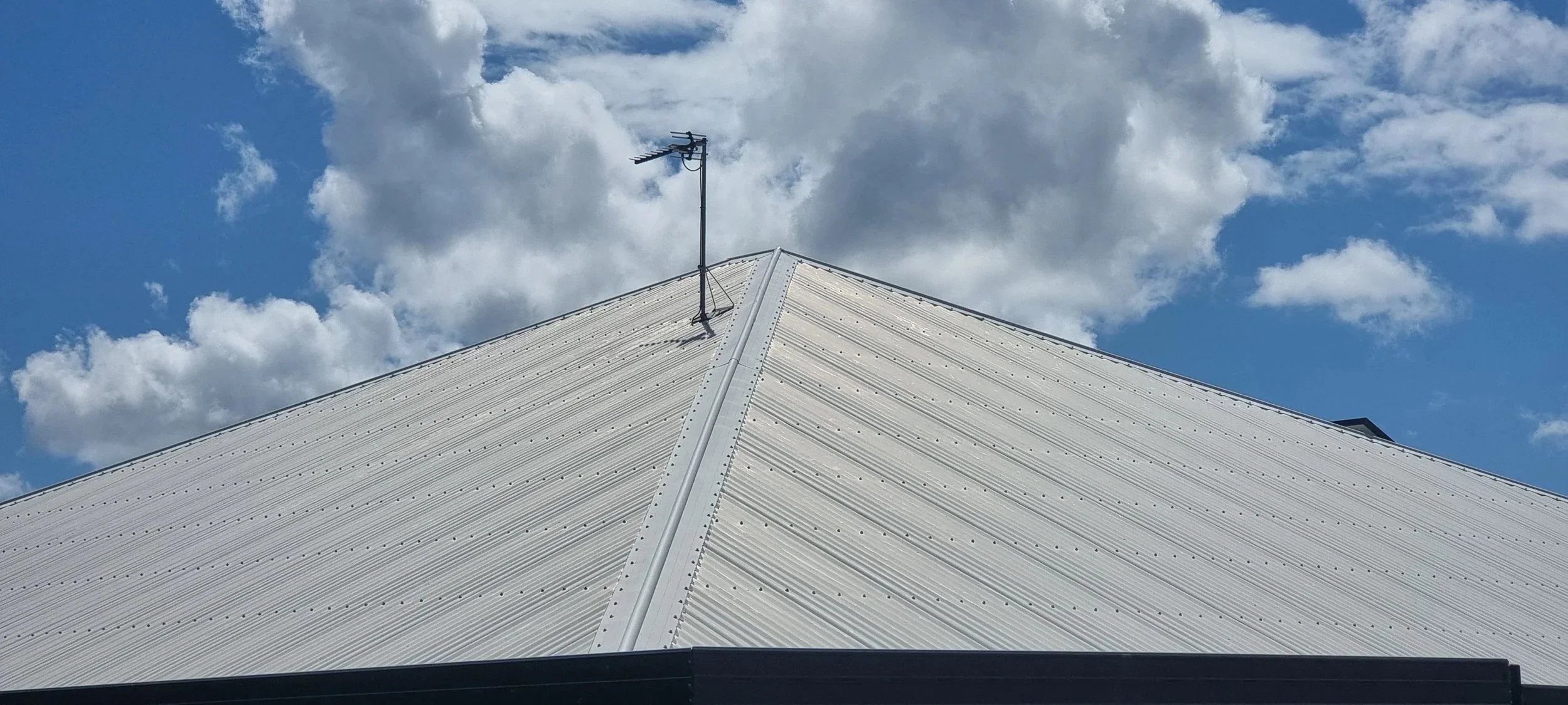 Close-up of a white metal roof with a TV antenna and a partly cloudy sky in the background.
