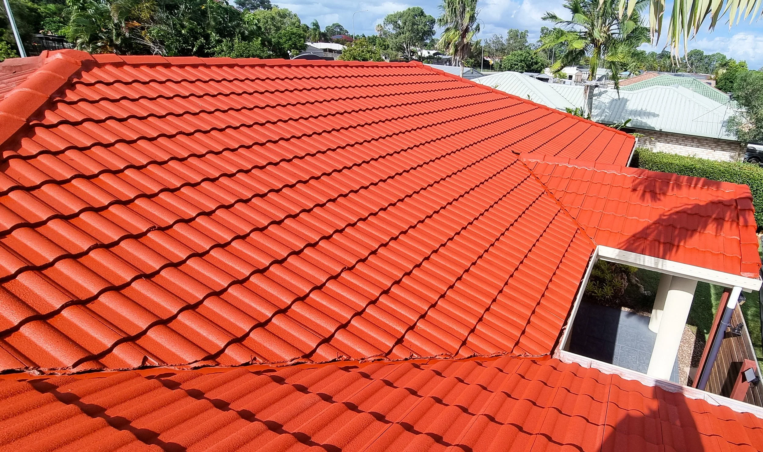 Red tiled roof of a house with backyard, trees, and neighboring houses in the background.