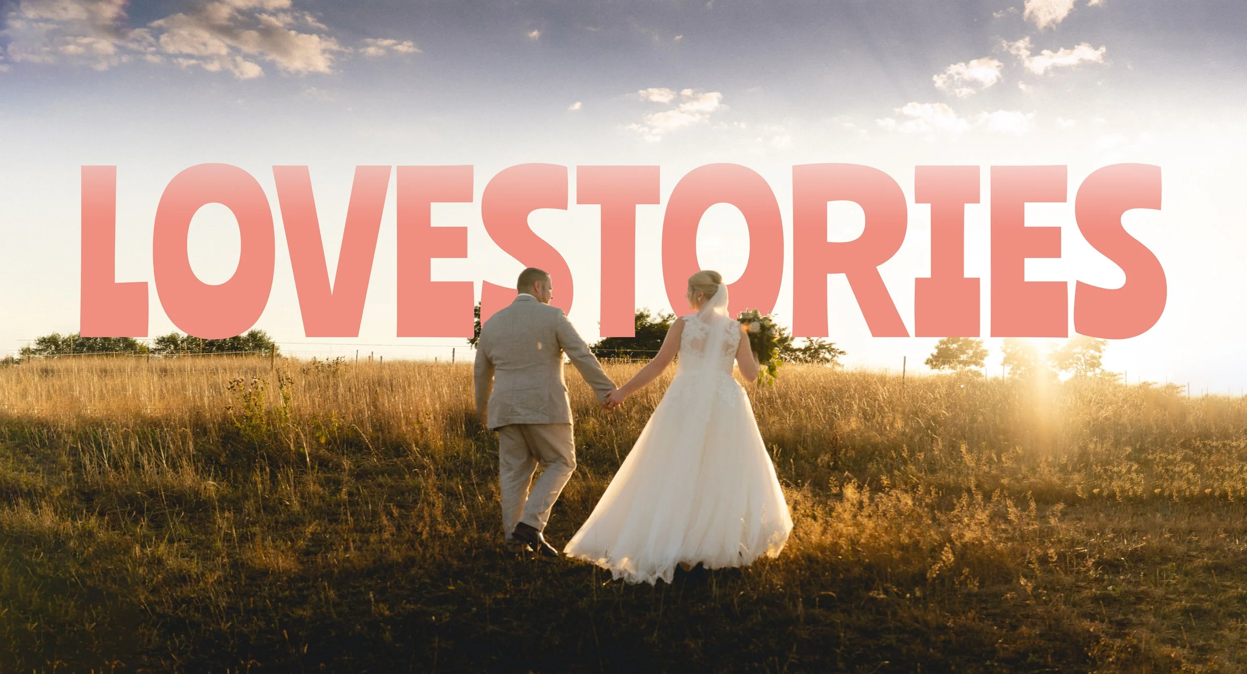 A bride and groom holding hands and walking in a field during sunset, with the word "LOVESTORIES" in large pink letters across the sky.