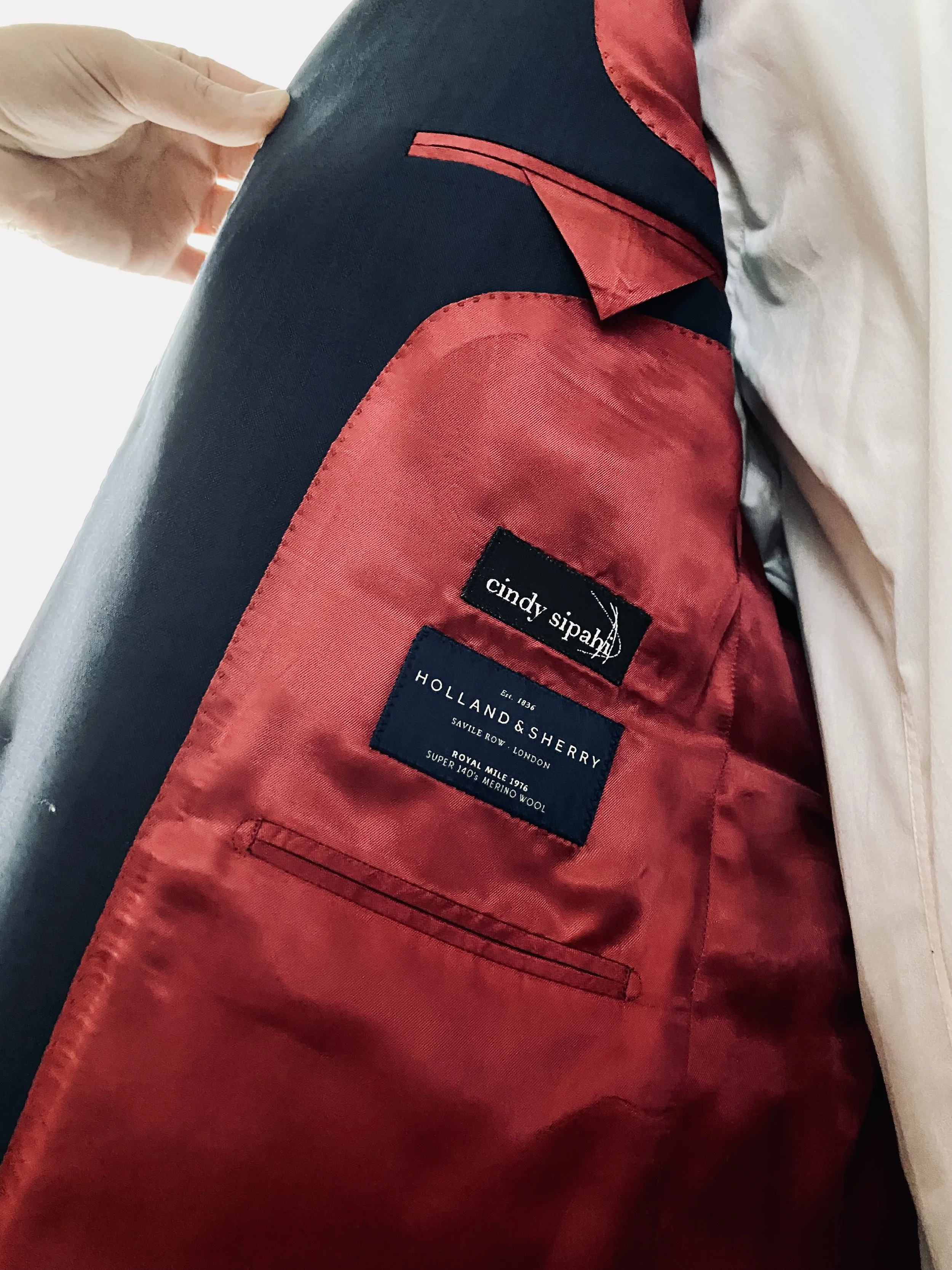 Close-up of the interior lining of a blazer, showing labels for Cindy Sipah and Holland & Sherry fabric, with red satin-like fabric and a small pocket.