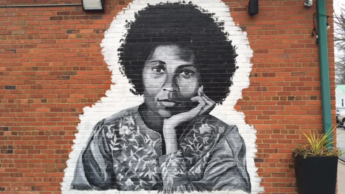 Black and white mural of bell hooks, resting her chin on her hand, painted on a brick wall.