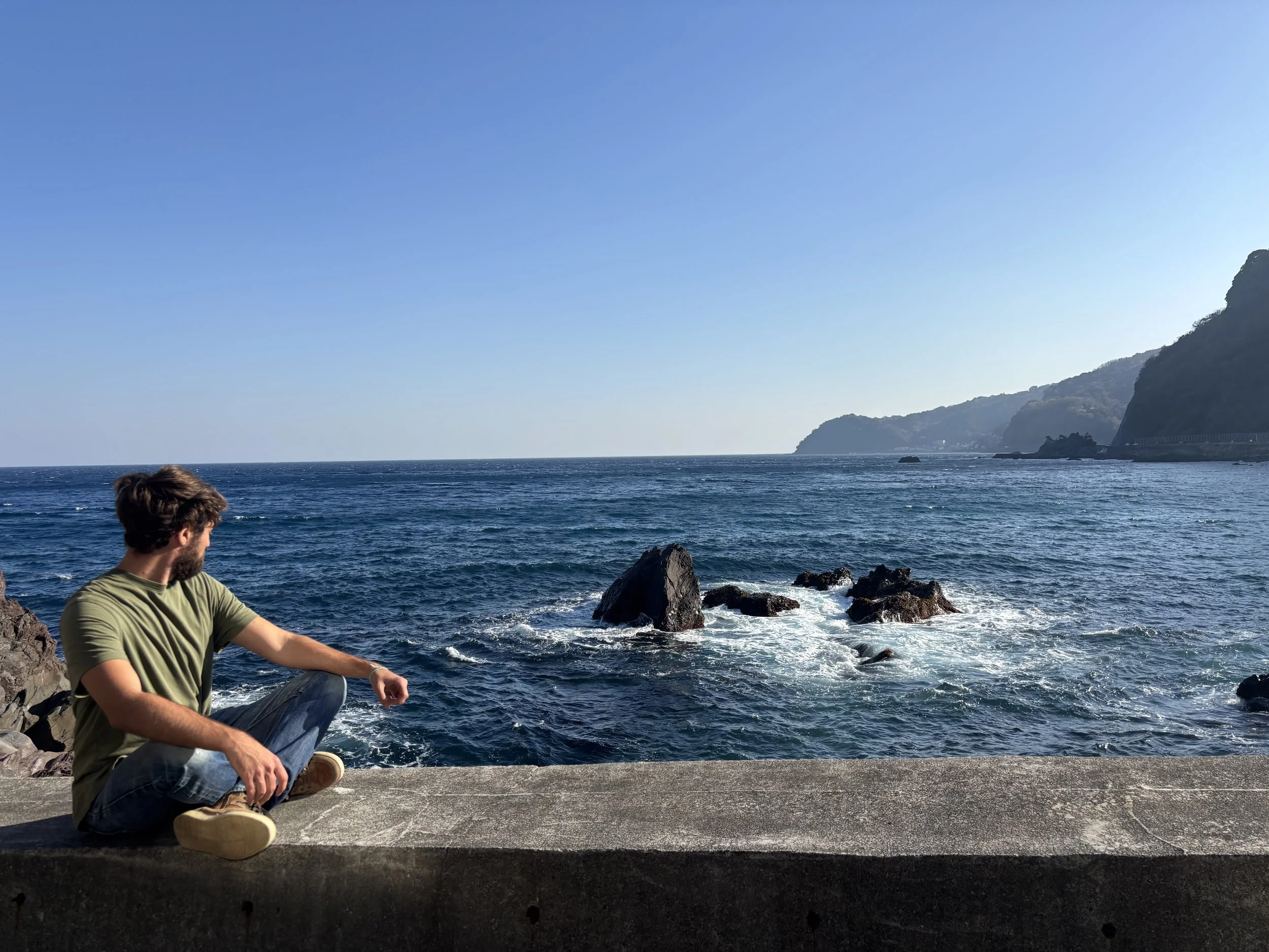 meditator sitting cross-legged looks out at a serene coastal view