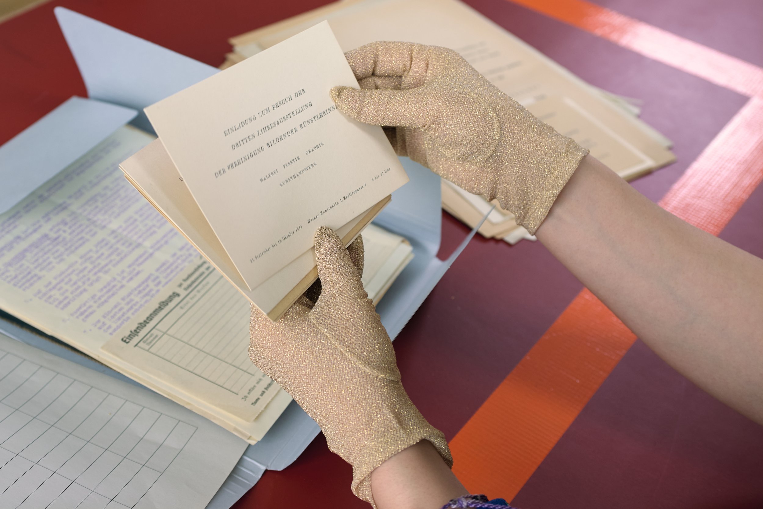 A person wearing glittery gloves is flipping through a small booklet or program, with stacks of papers or booklets on a table nearby.