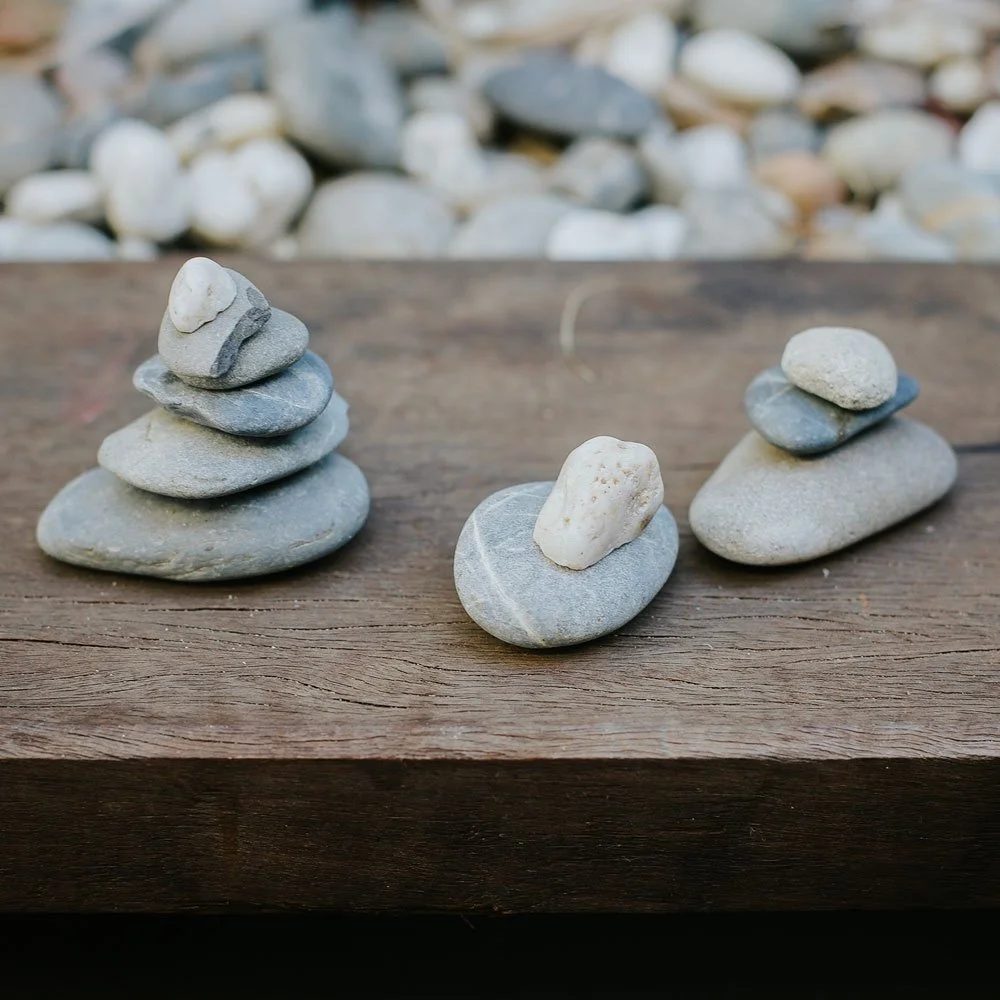 Three small rock stacks on a wooden surface with a gravel background.