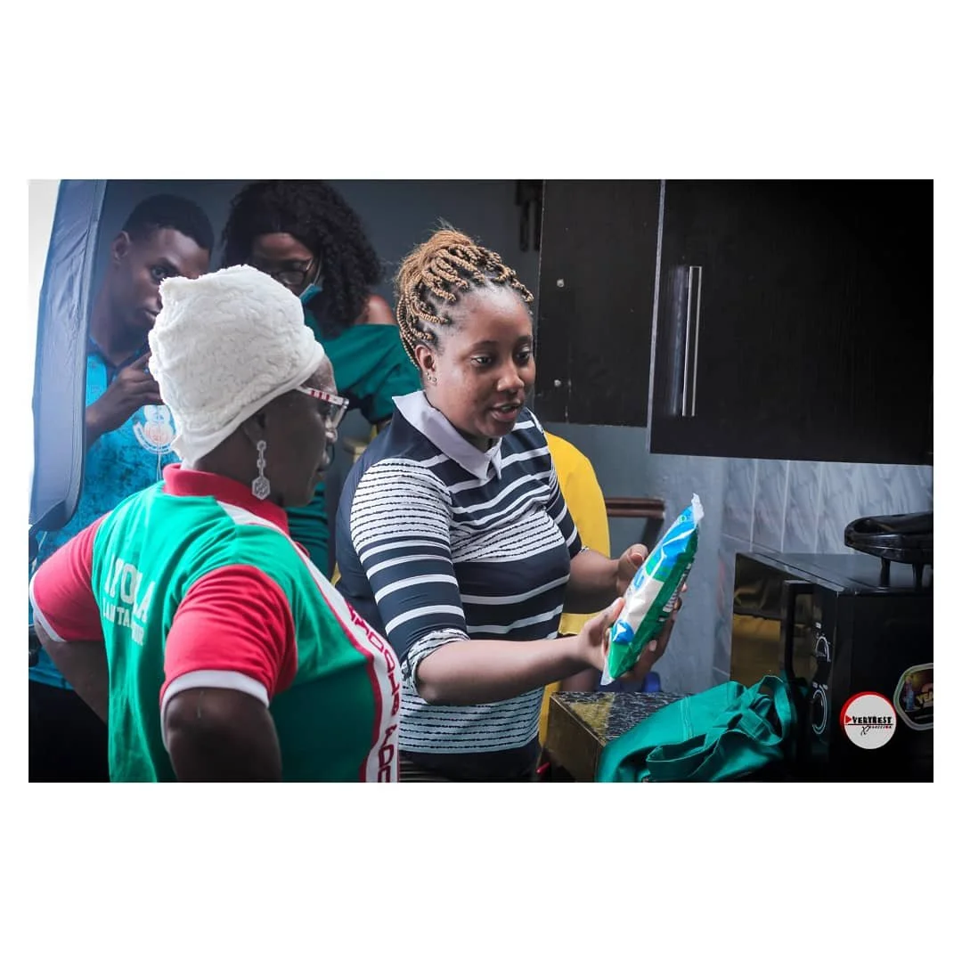 Group of women indoors, one woman showing a packet to others, with a microwave oven nearby.