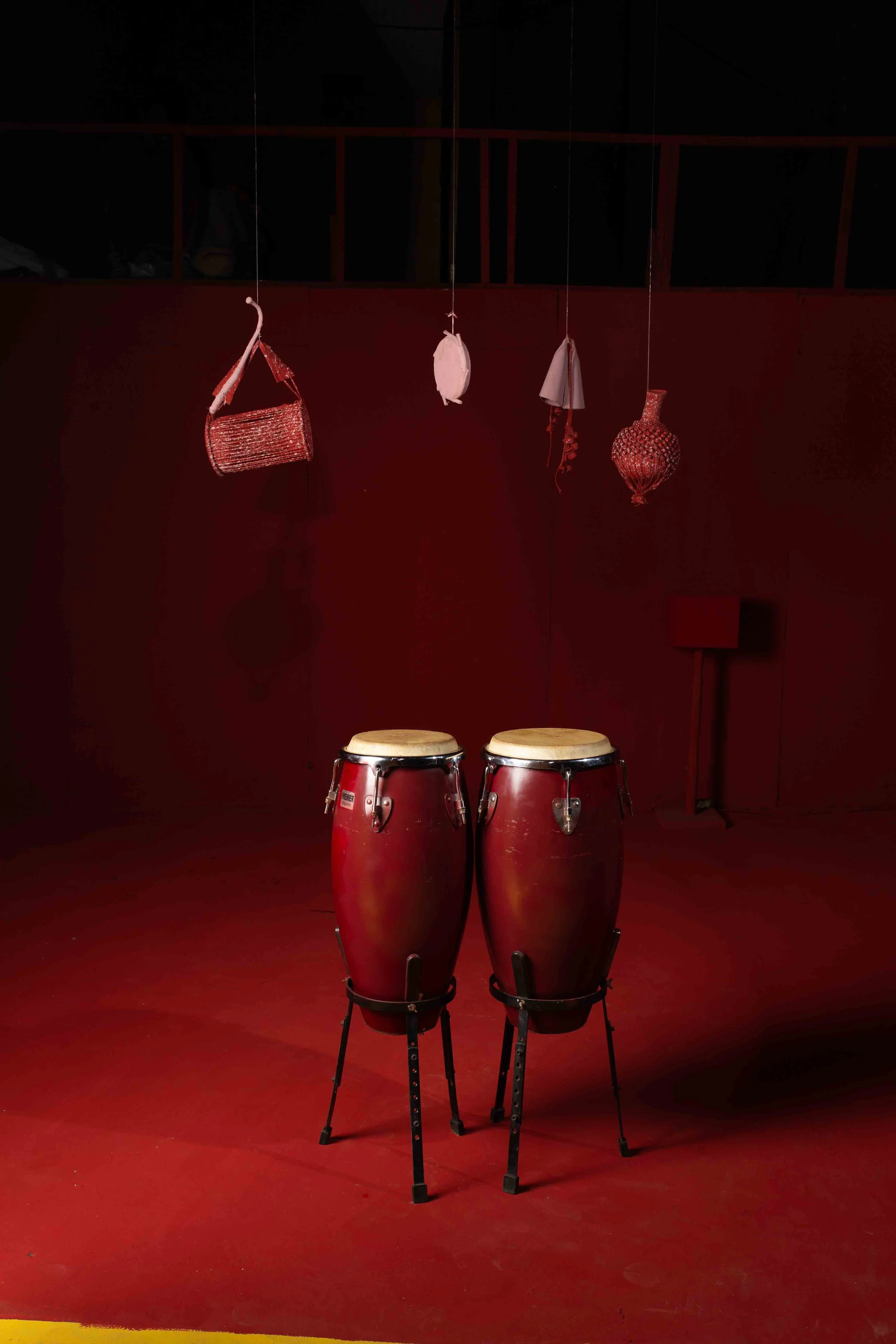 Pair of red conga drums on stands in a dimly lit room with red walls and hanging decorative objects.