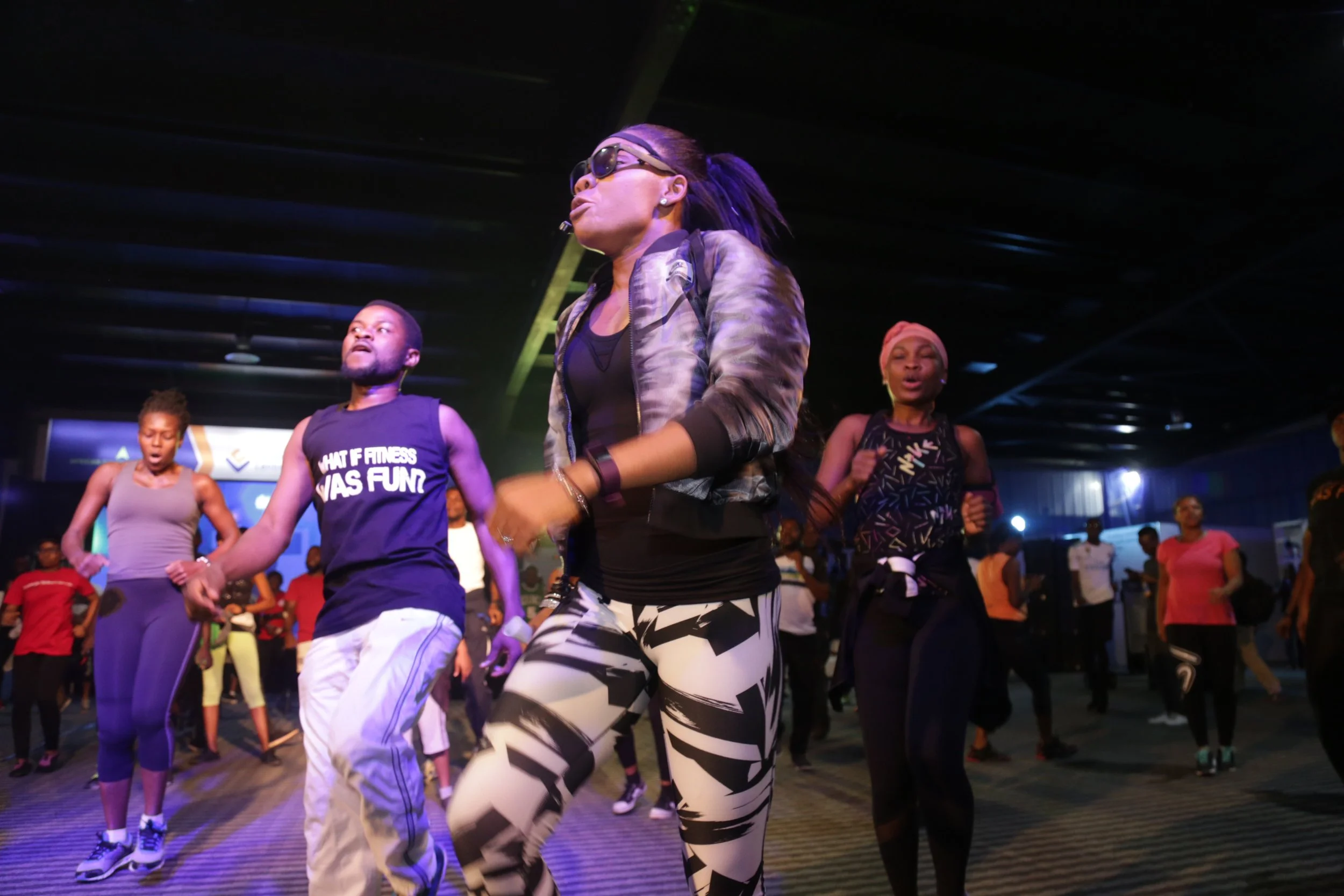 People participating in a group fitness class in a dark indoor gym, dancing and exercising together.