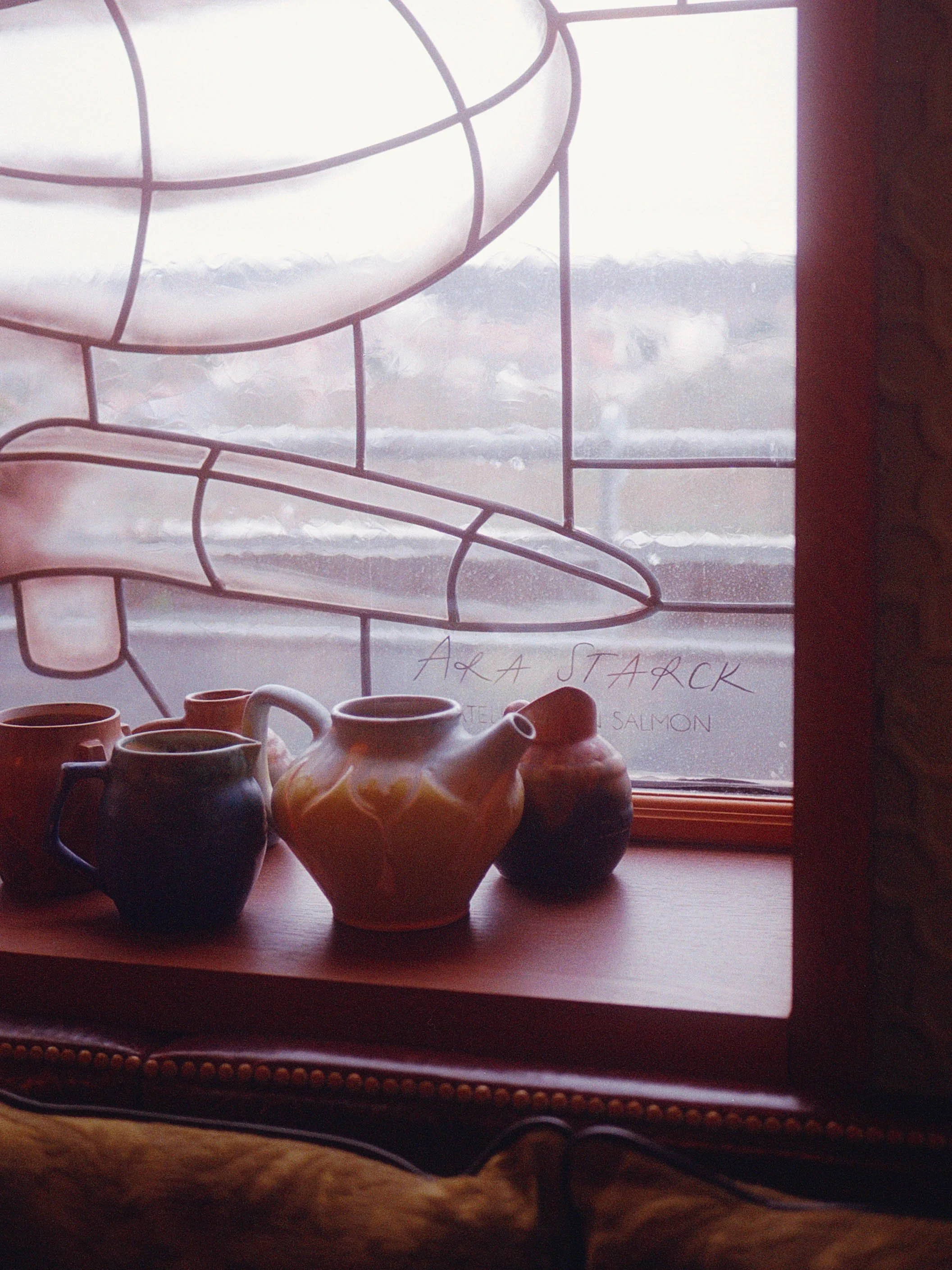 Vase en céramique et tasses sur une fenêtre en bois avec dessin d'un doigt en verre coloré et écriture.