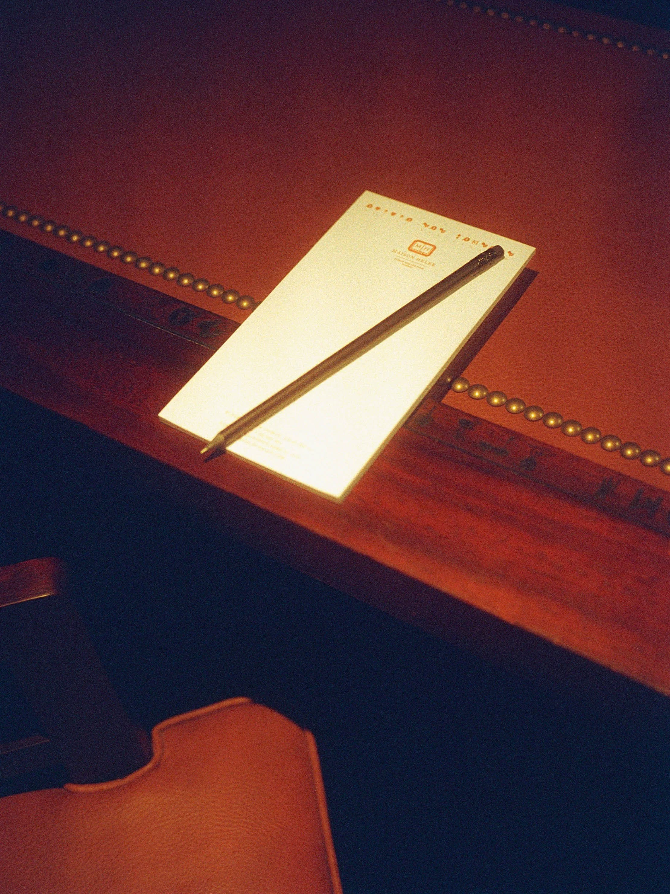 Une fiche ou un bloc-note blanc avec un stylo noir posé dessus, placé sur une table en bois avec une bordure en métal doré.