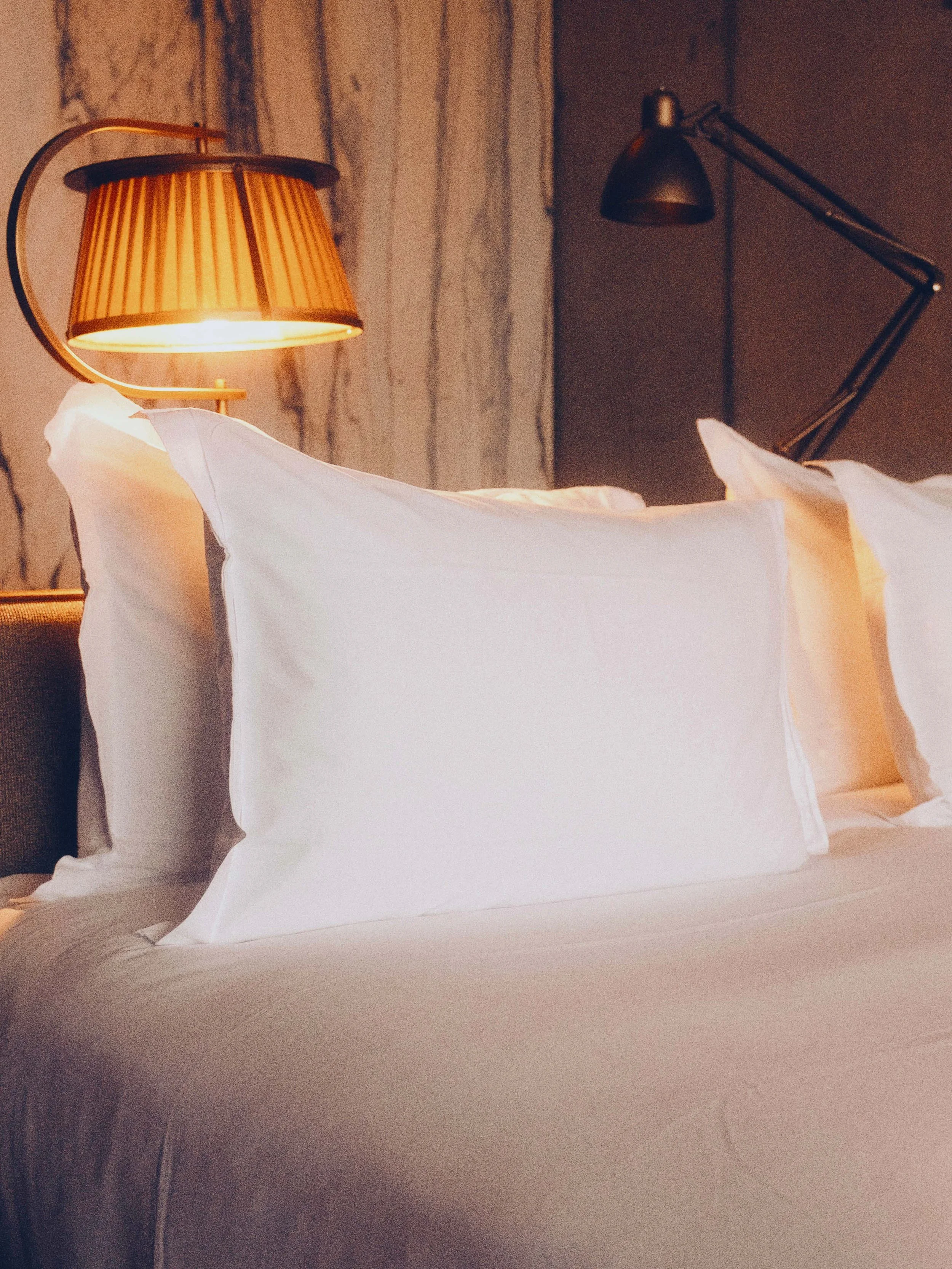 Lits avec des oreillers blancs et lampes de lecture suspendues, ambiance chaleureuse dans une chambre de l'hotel Heler à Metz.