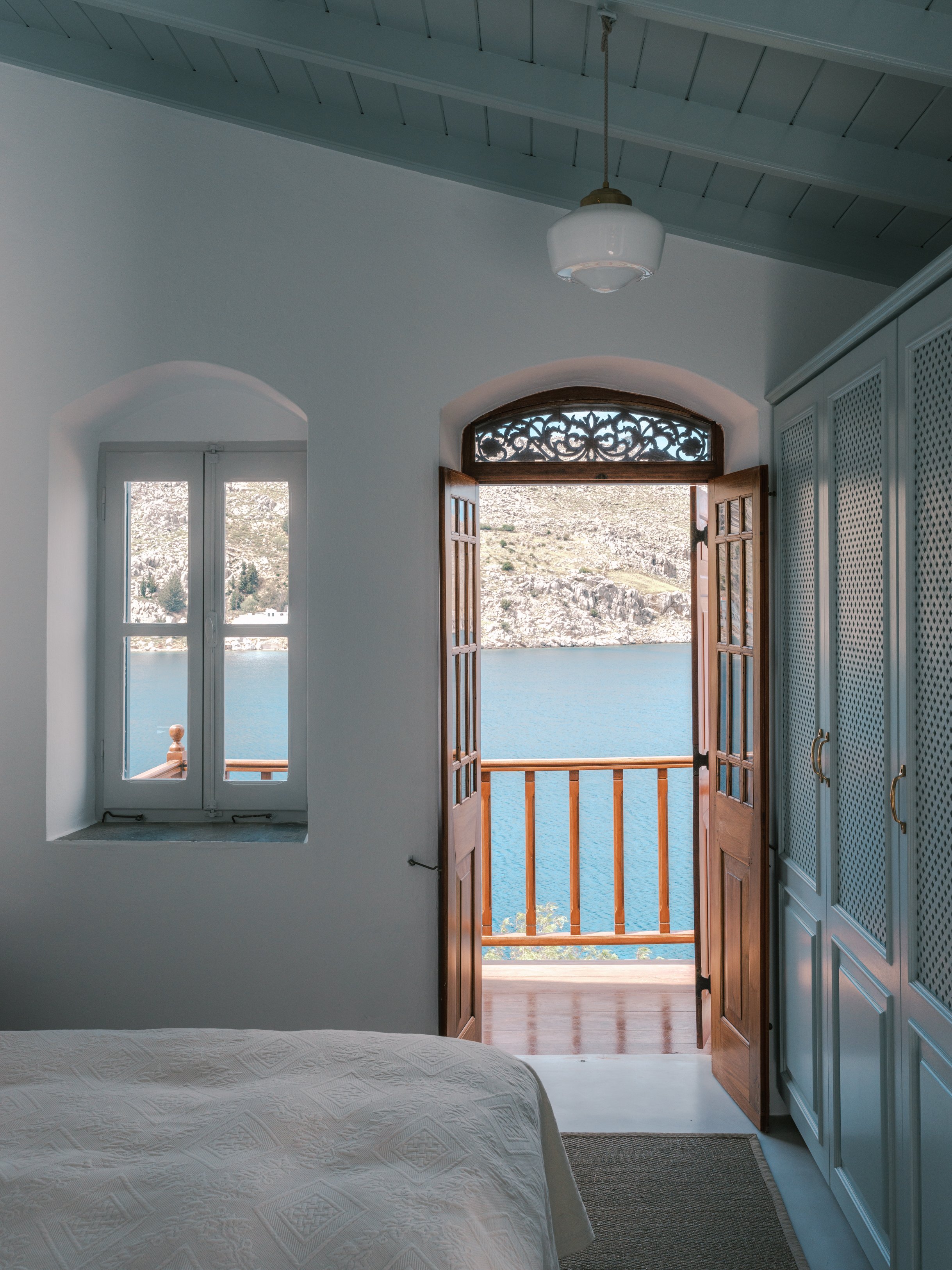 Eos suite view from inside looking out to a balcony with open wooden door doors, overlooking nimborio bay at the selene greece, symi