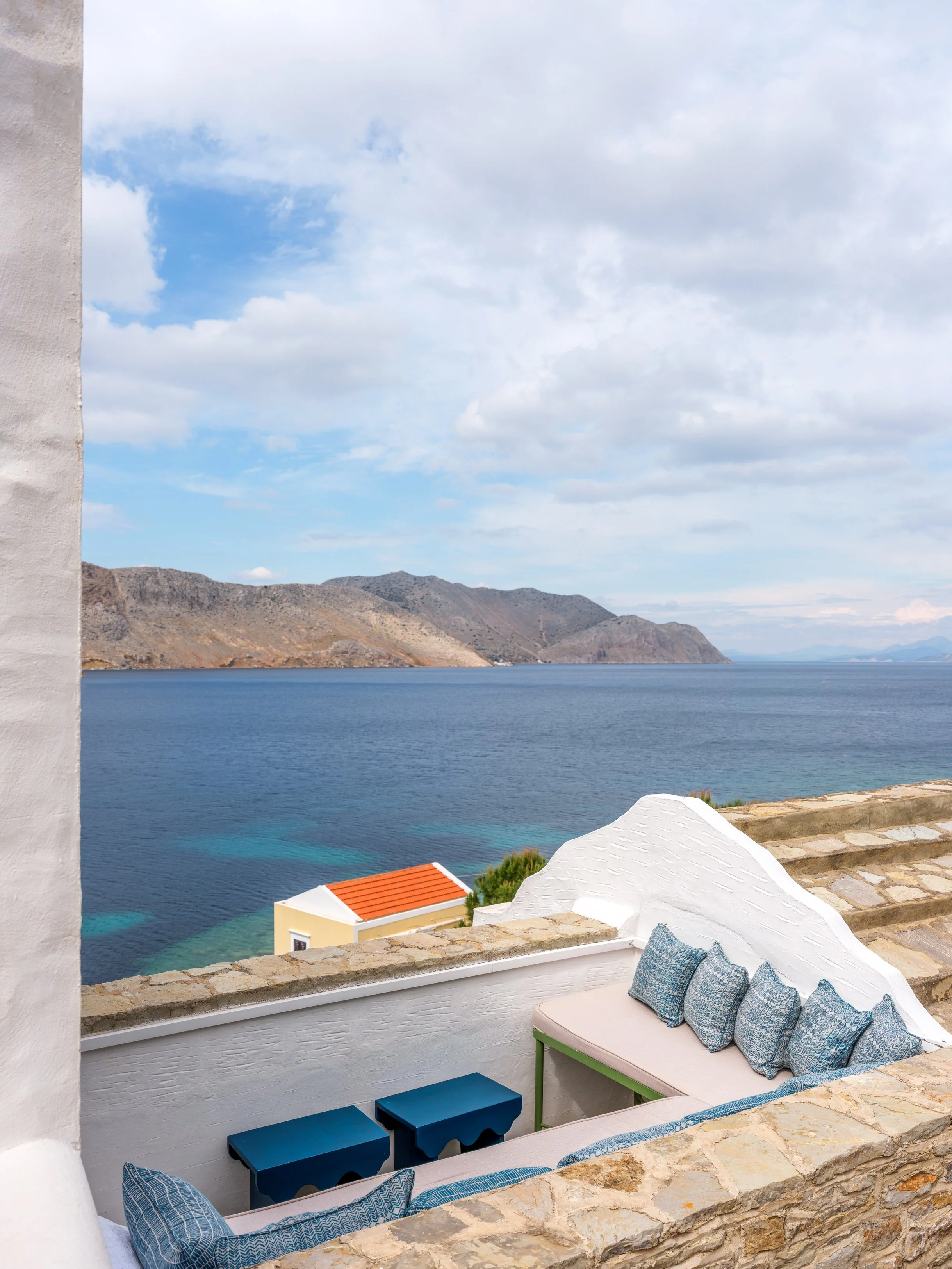 Eos roof terrace white walls, blue cushions on a fitted bench overlooking nimborio bay with mountains in the background at the selene greece, symi