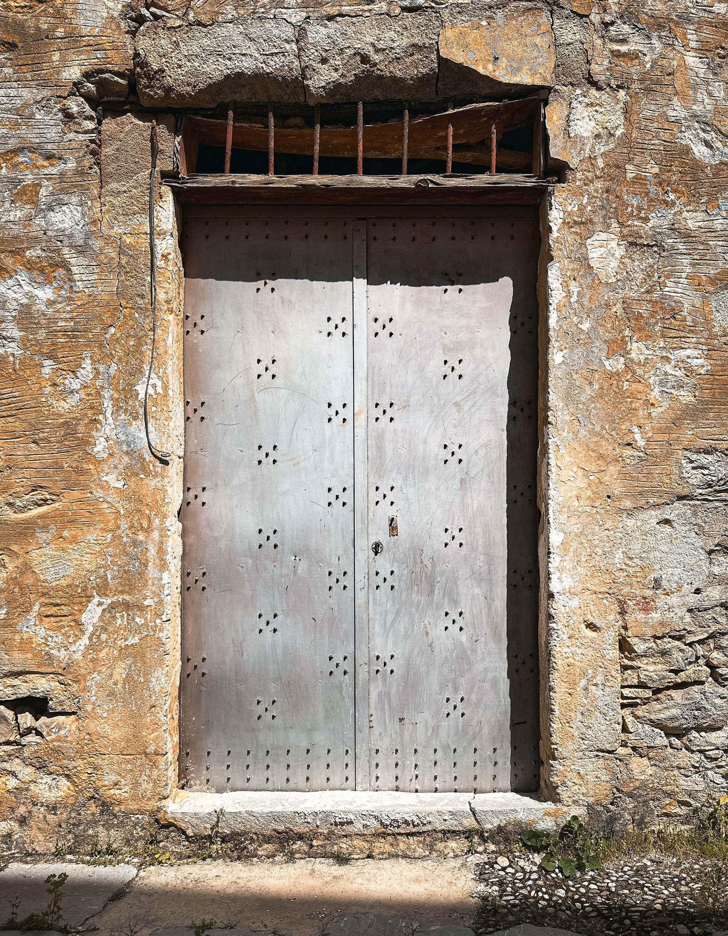 Close-up of an old, weathered metal door in Symi village set into a rough, textured stone wall with peeling plaster.