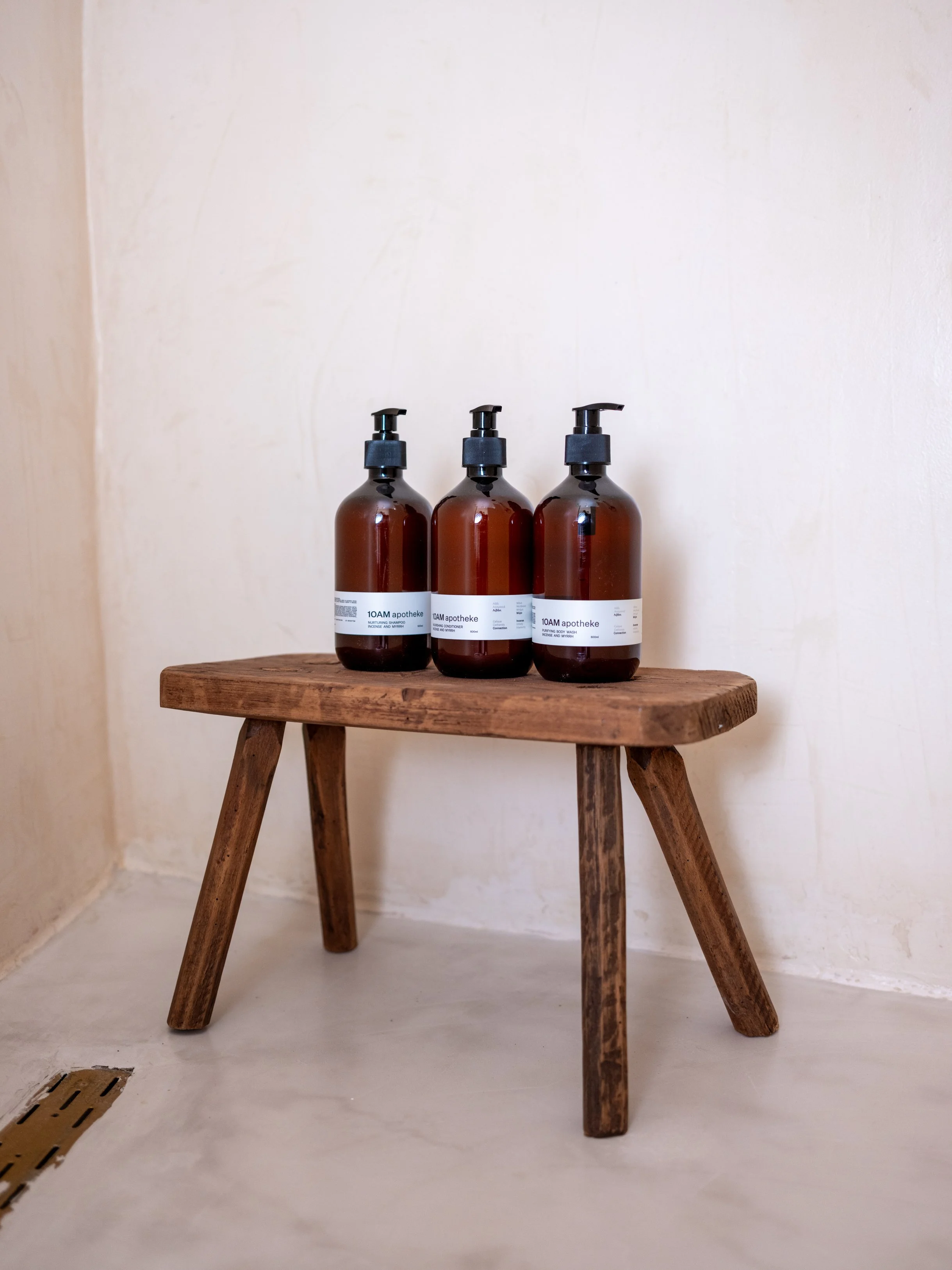 Three amber glass pump bottles from 10am apotheke on a rustic wooden stool at the selene greece, symi