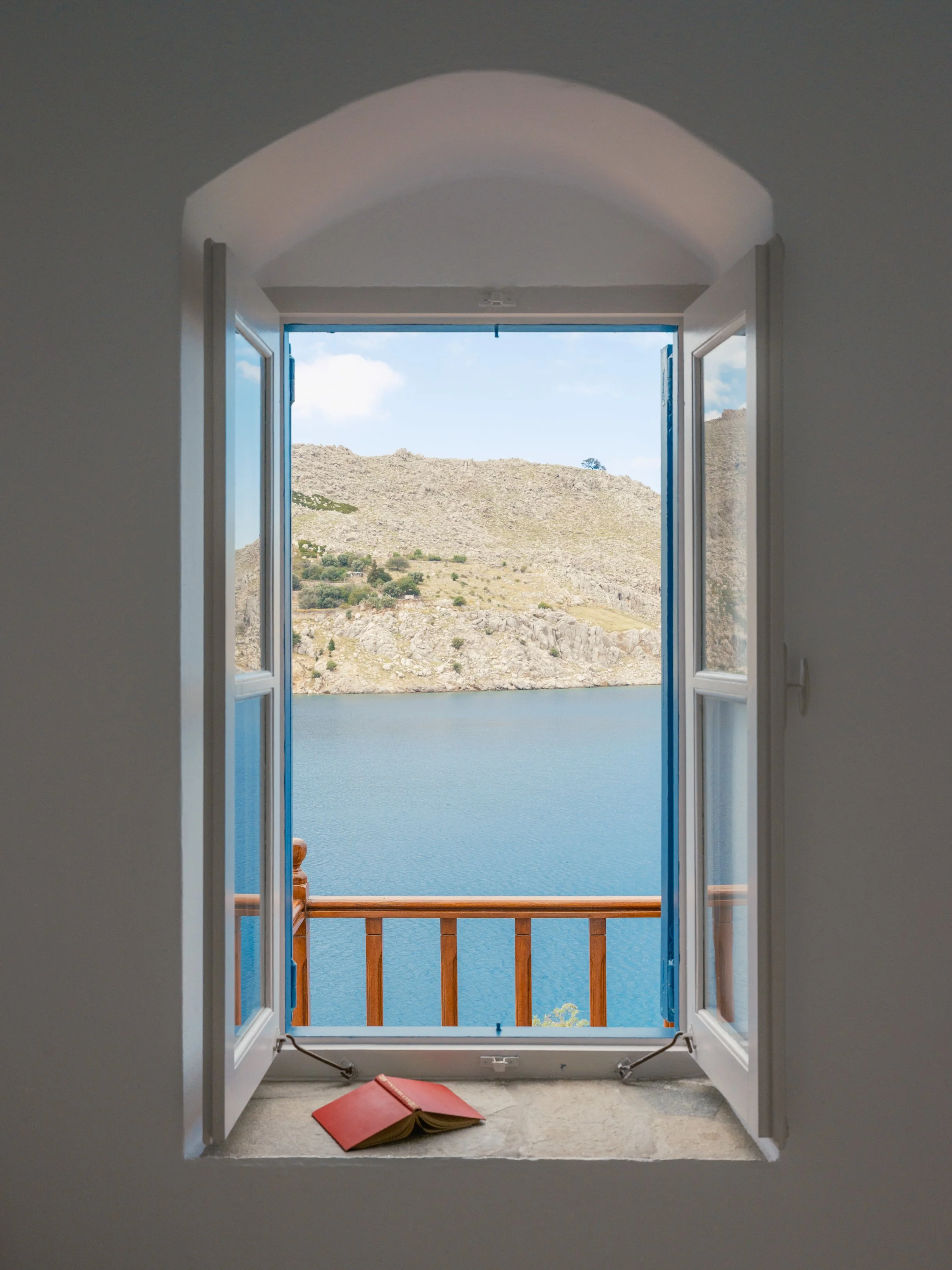 Eos suite open window with blue shutters looking out over nimborio bay and rocky hills in the distance at the selene greece, symi