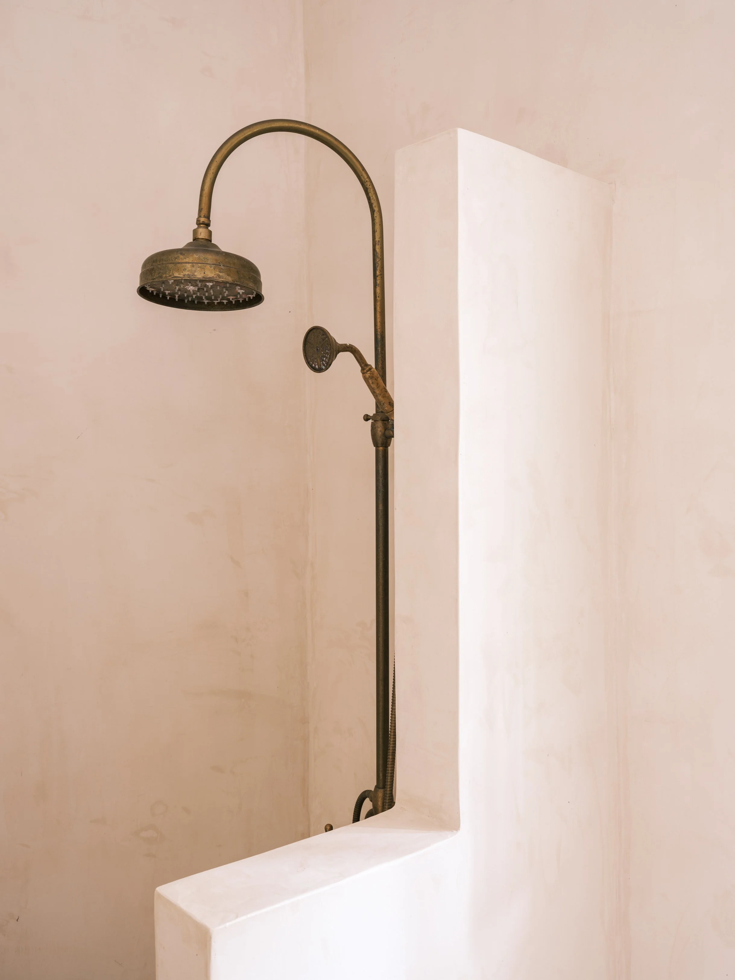 Gaia room vintage brass shower mounted on a wall with a white curved platform underneath at the selene greece, symi
