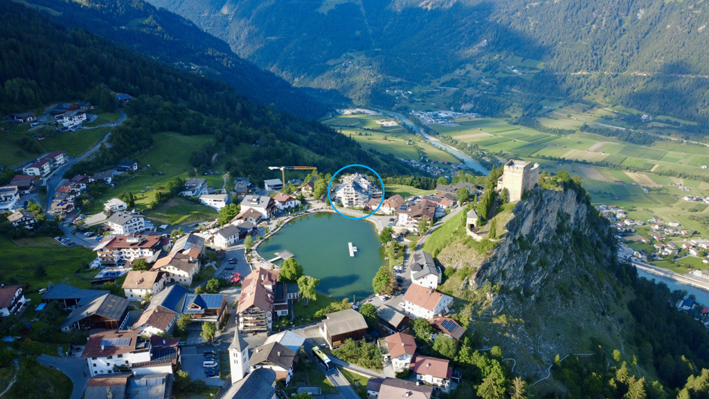 Luftaufnahme auf Ladis mit der historischen Burg, umliegenden Bergen und Feldern und mitten drin die Mietwohnanlage homelodge