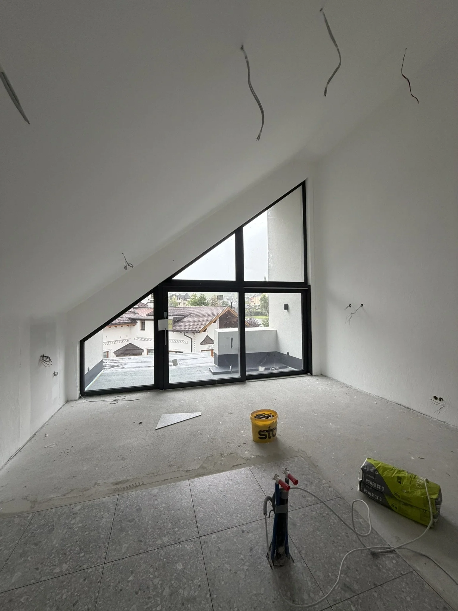 Wohnraum mit Dachschräge und bodentiefem Fenster im Rohbauzustand