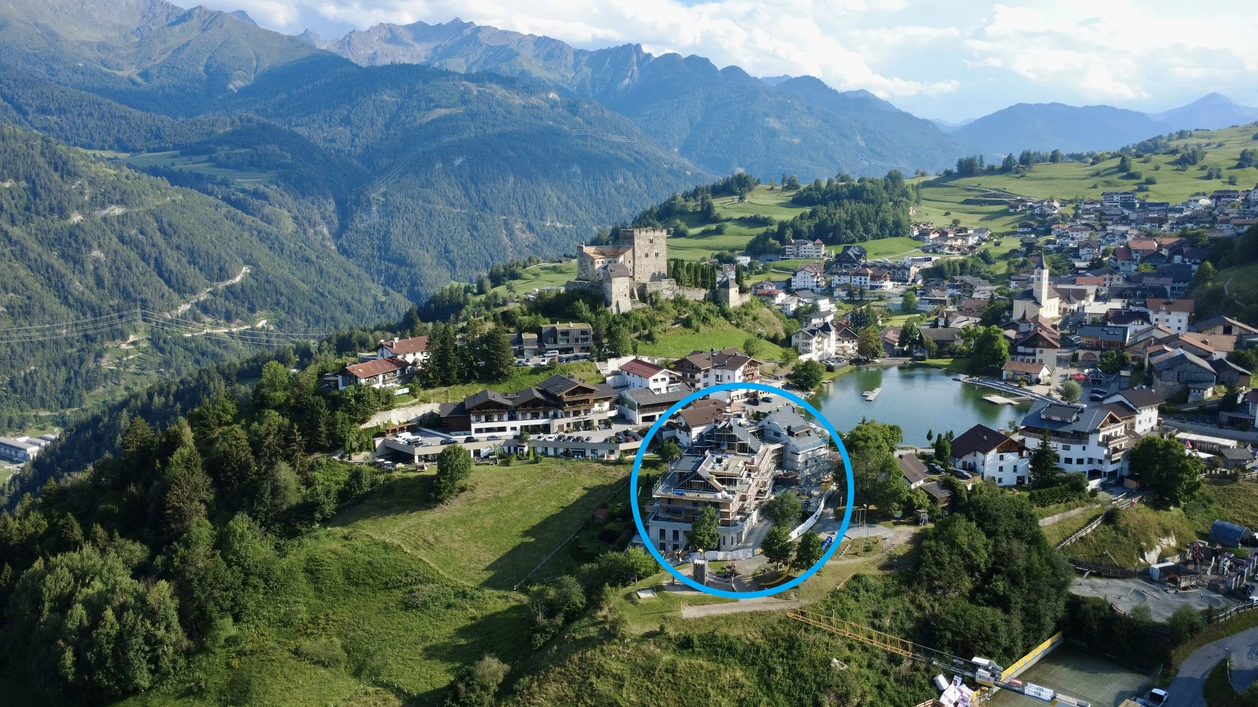 Das Bergdorf Ladis in den Alpen mit Weiher, umgeben von grünen Hügeln. Im Vordergrund befindet sich die homelodge mit freiem Blick ins Inntal